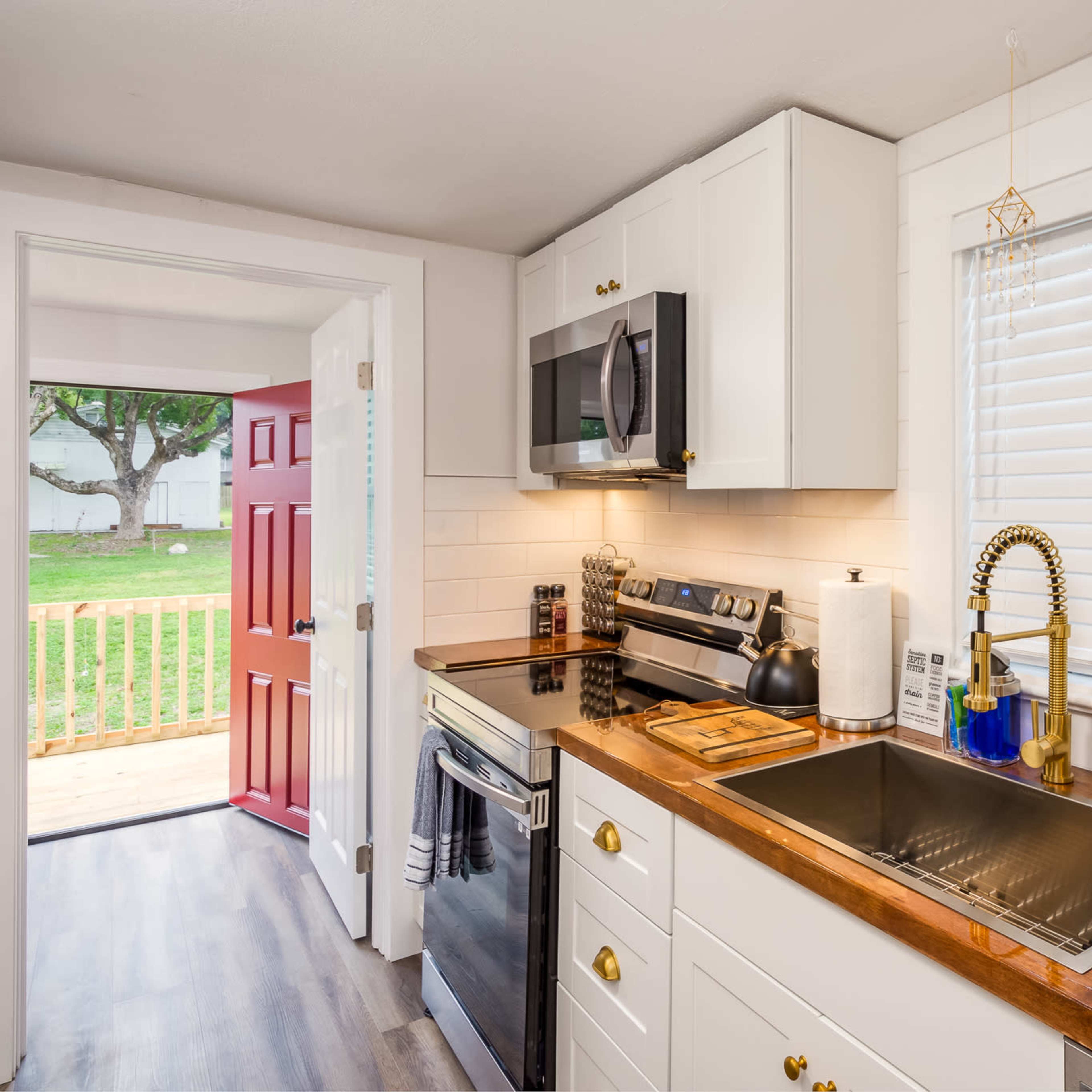 A modern kitchen features white cabinets, stainless steel appliances, and a view of a red door opening to an outdoor area.