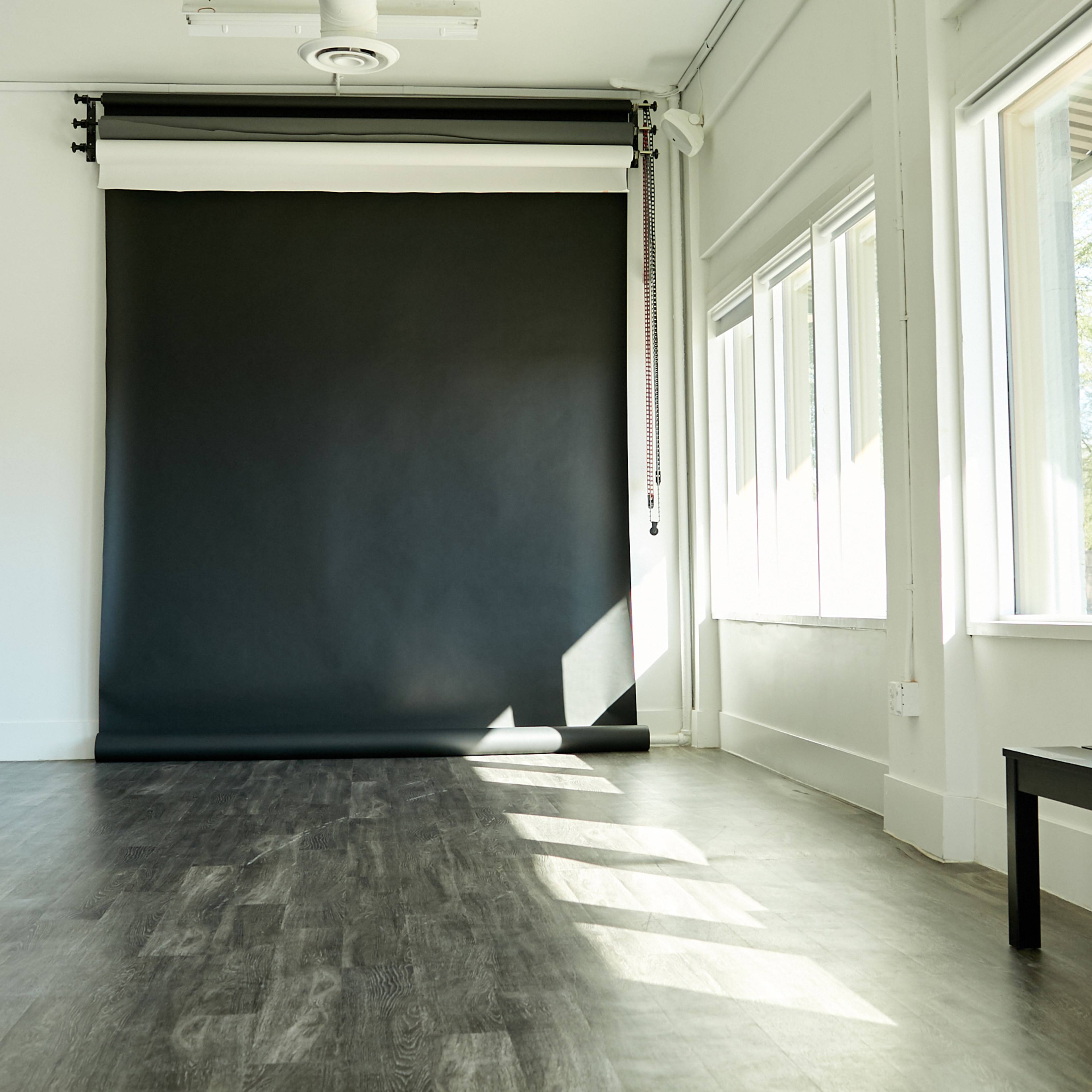 A spacious room features a large black backdrop and several windows allowing natural light to enter.