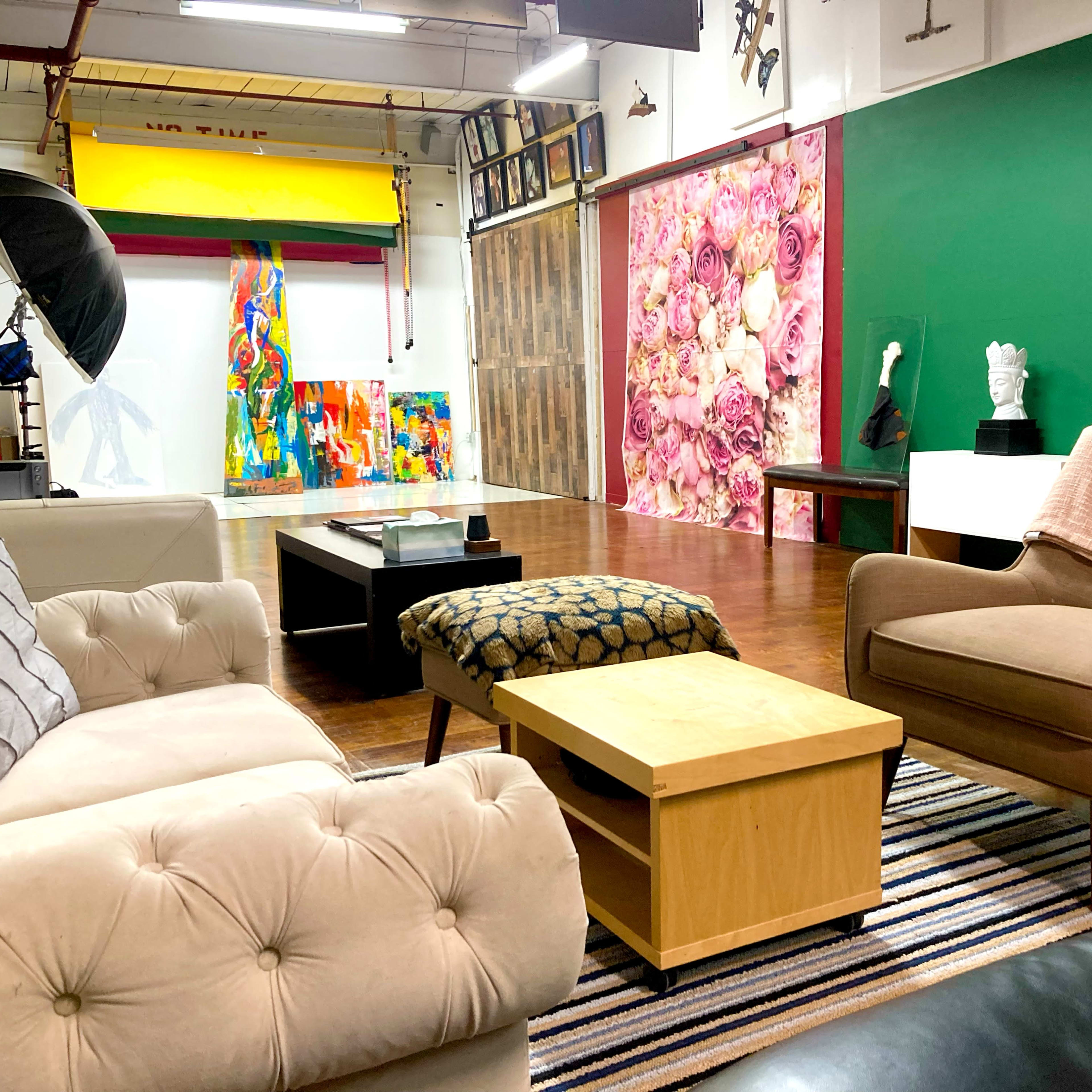 A spacious art studio featuring various colorful artworks, different seating arrangements, and a backdrop with a floral design.
