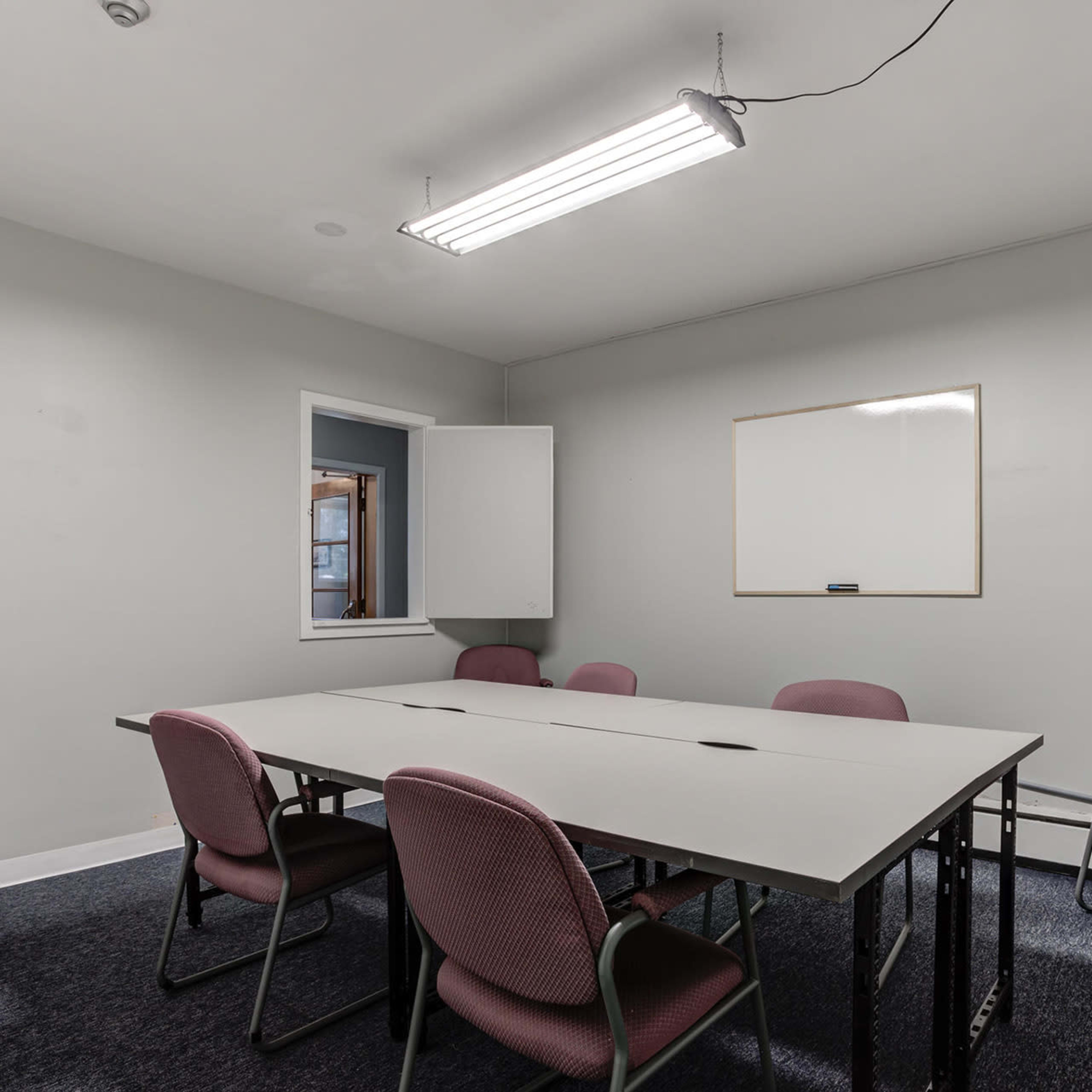 A small meeting room features a rectangular table surrounded by six chairs and a whiteboard mounted on the wall.