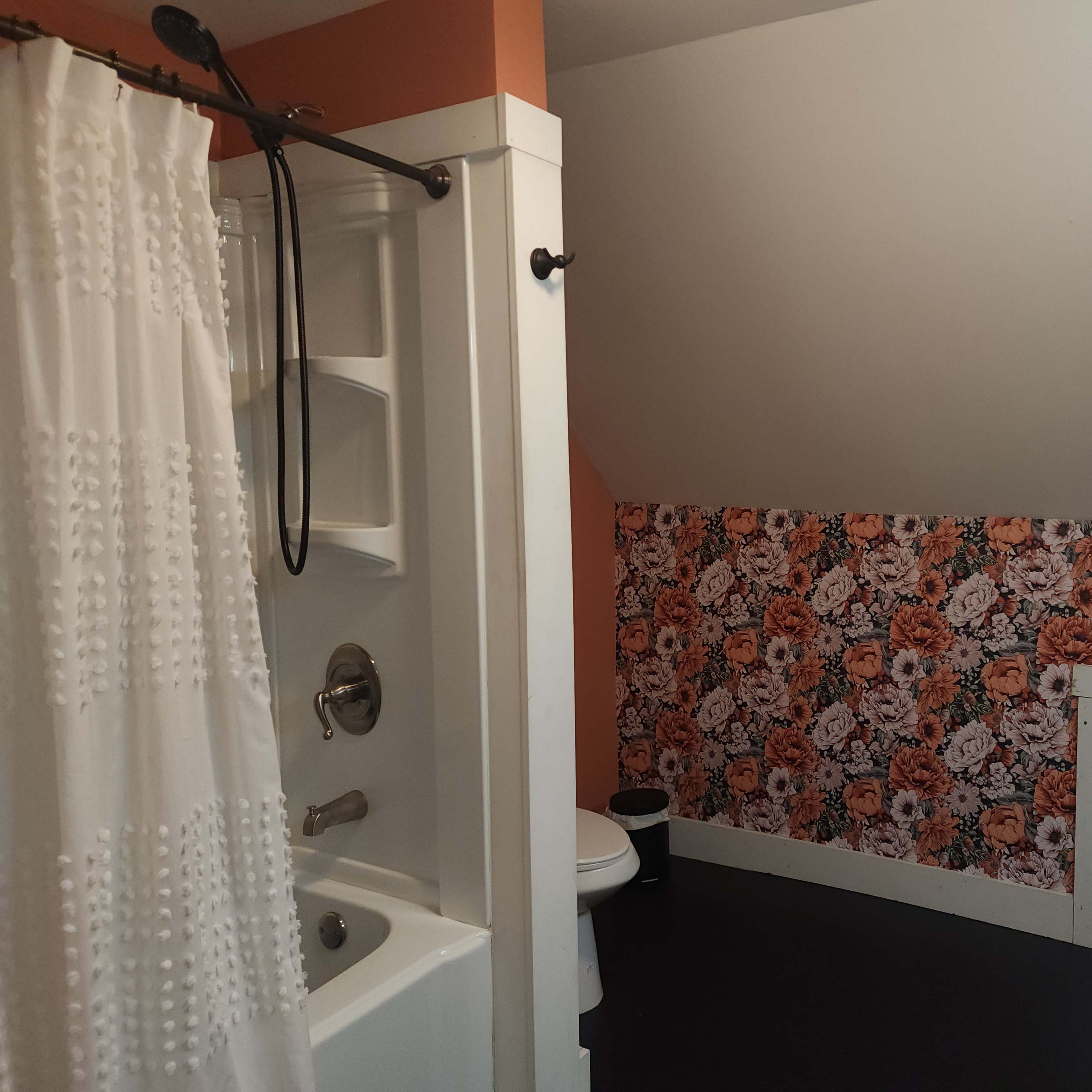 A bathroom with a shower curtain, a bathtub, a toilet, and floral wallpaper on one wall.