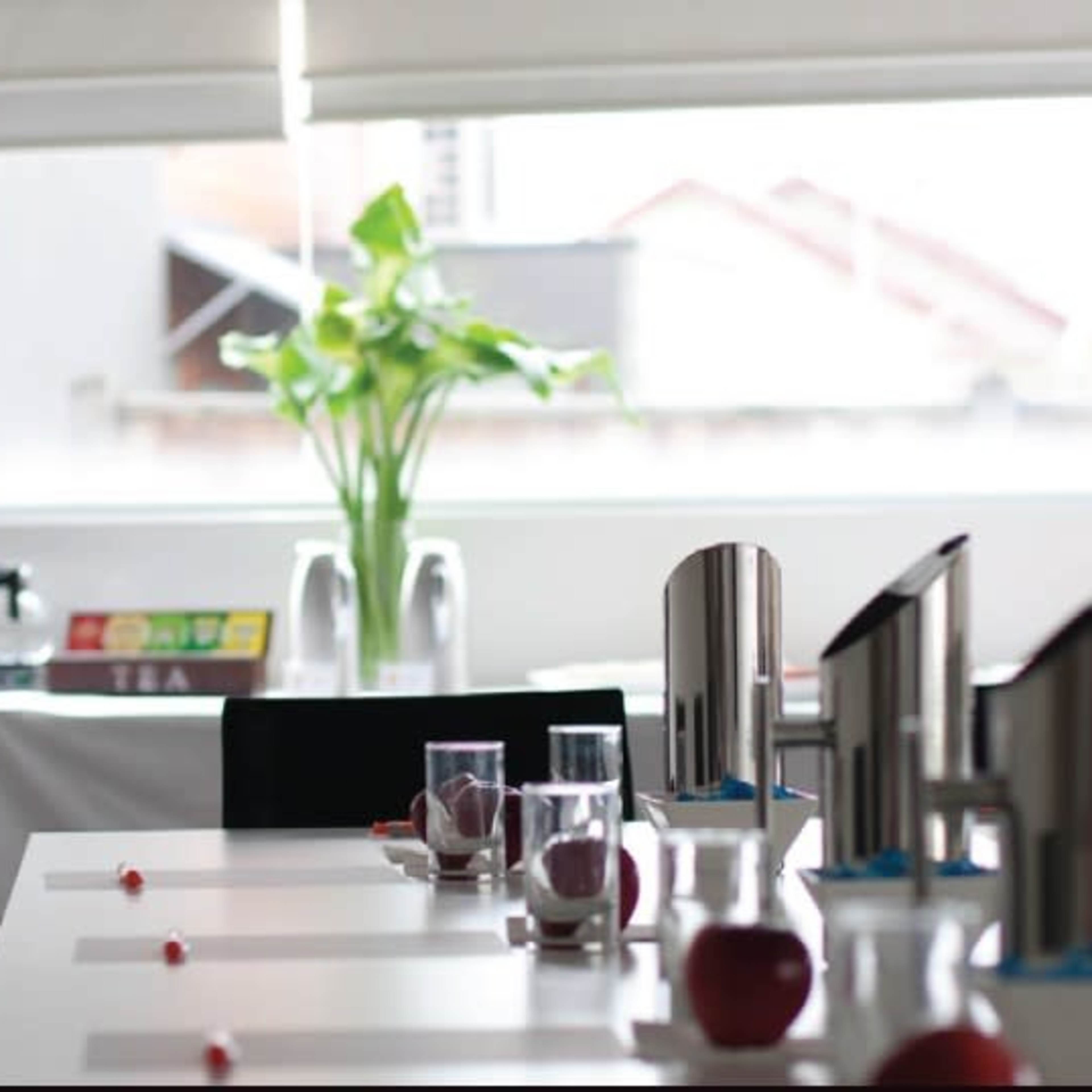 A modern dining room features neatly arranged tables with silver water pitchers, clear glasses, and red apples, along with a visible buffet setup in the background.