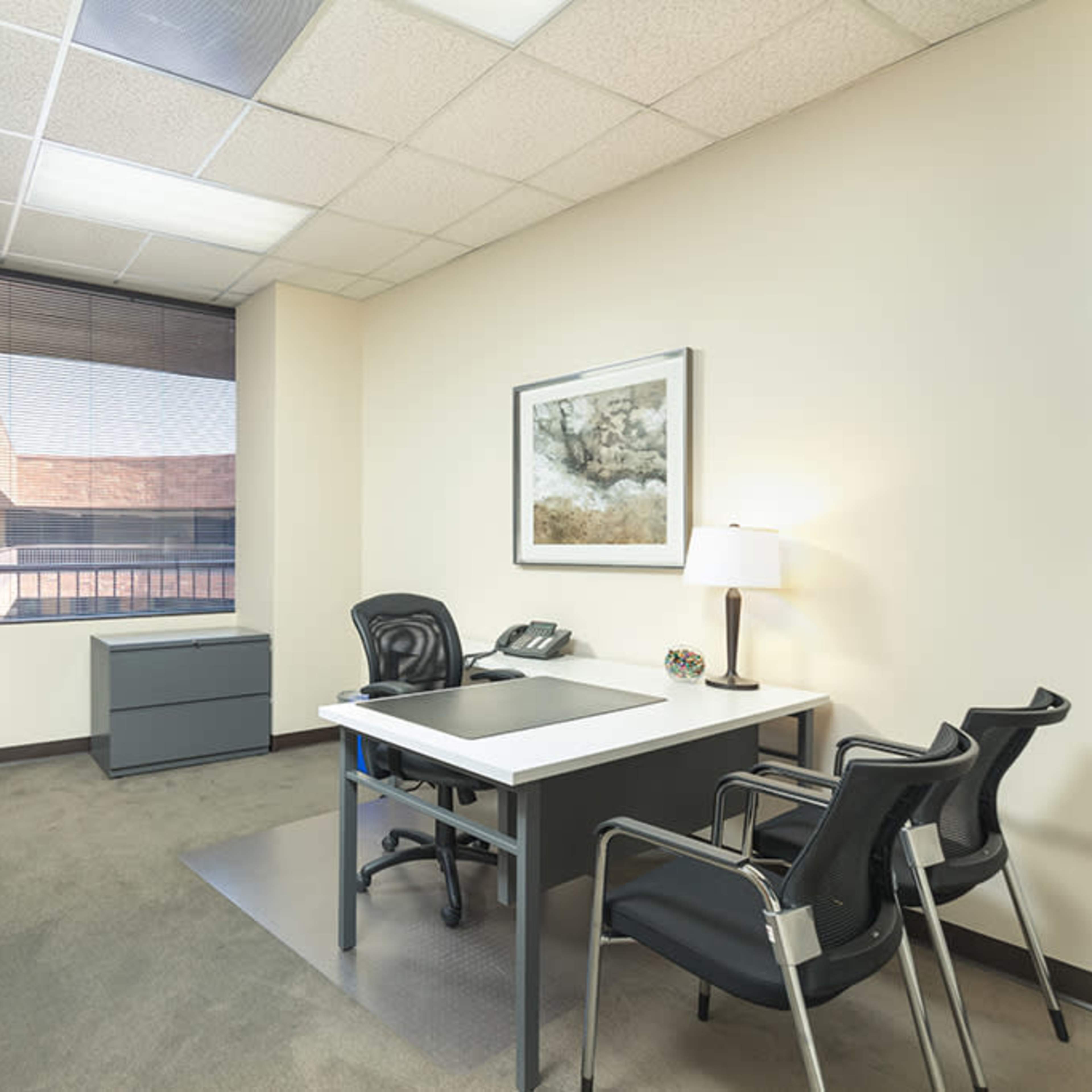 A modern office space featuring a desk with two chairs, a sofa, and a window with blinds.