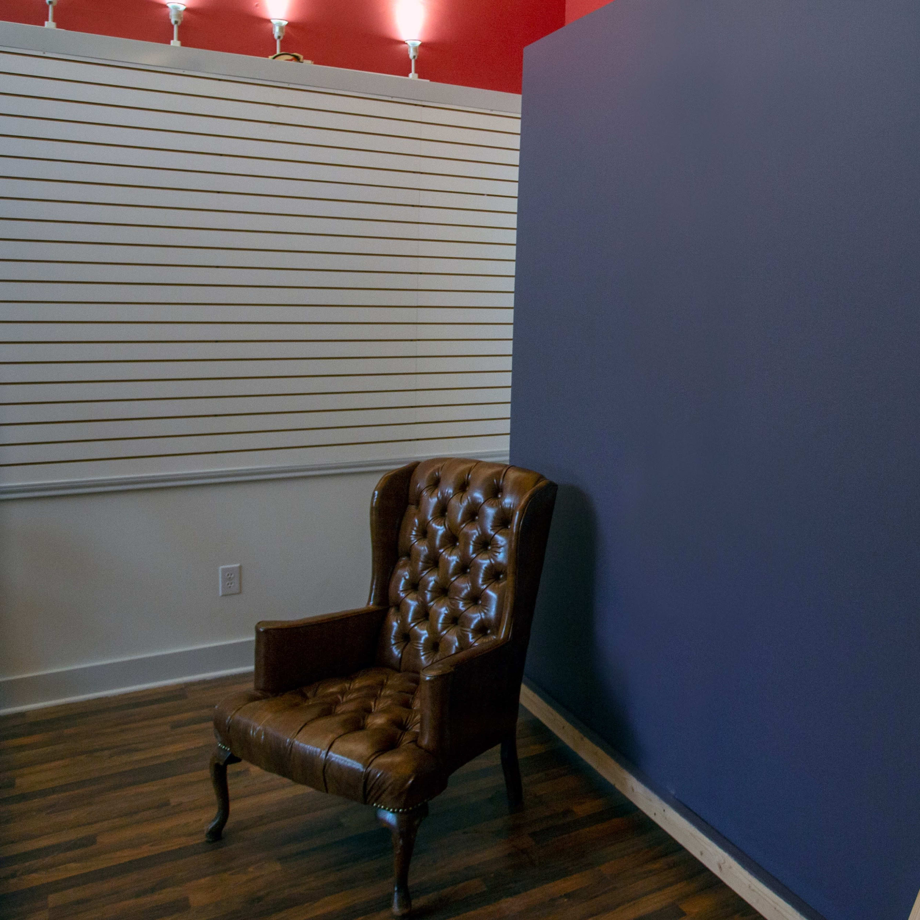 A brown leather chair is positioned next to a blue wall supported by a wooden frame in a room with hardwood flooring.