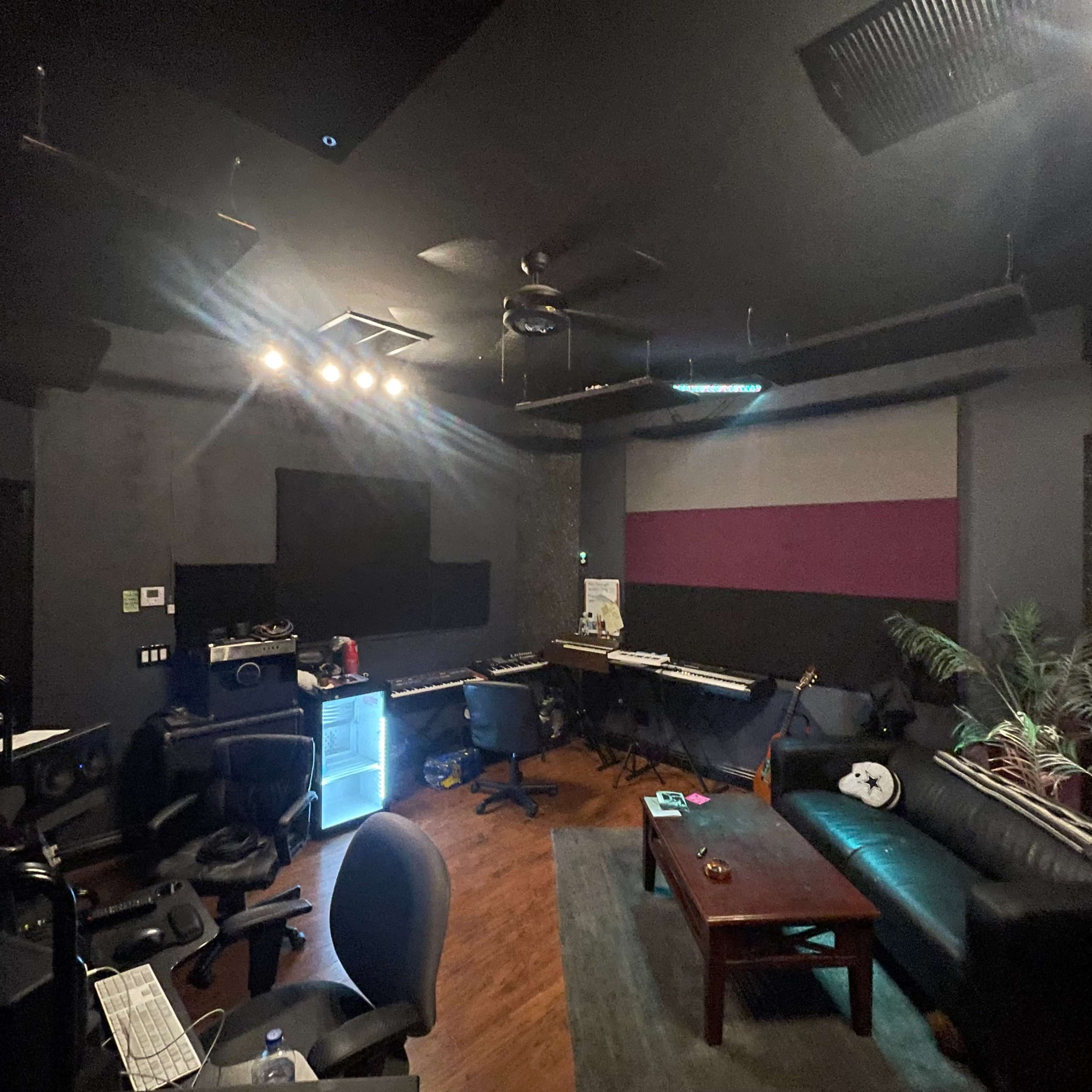 A music studio with dark walls, a desk with musical equipment, and a leather sofa in a corner.