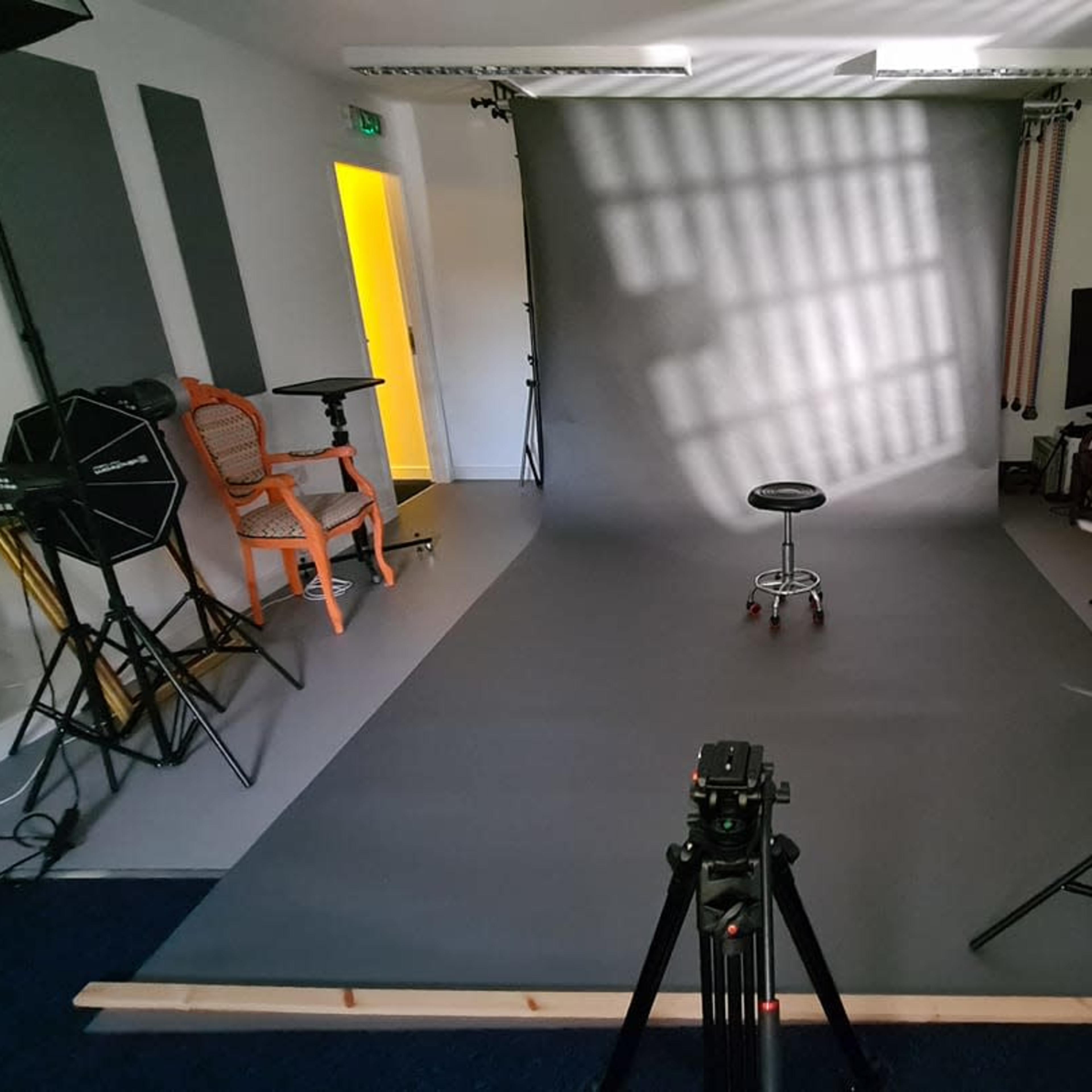 A photography studio features a gray backdrop, a stool in the center, and various lighting equipment set up around the space.