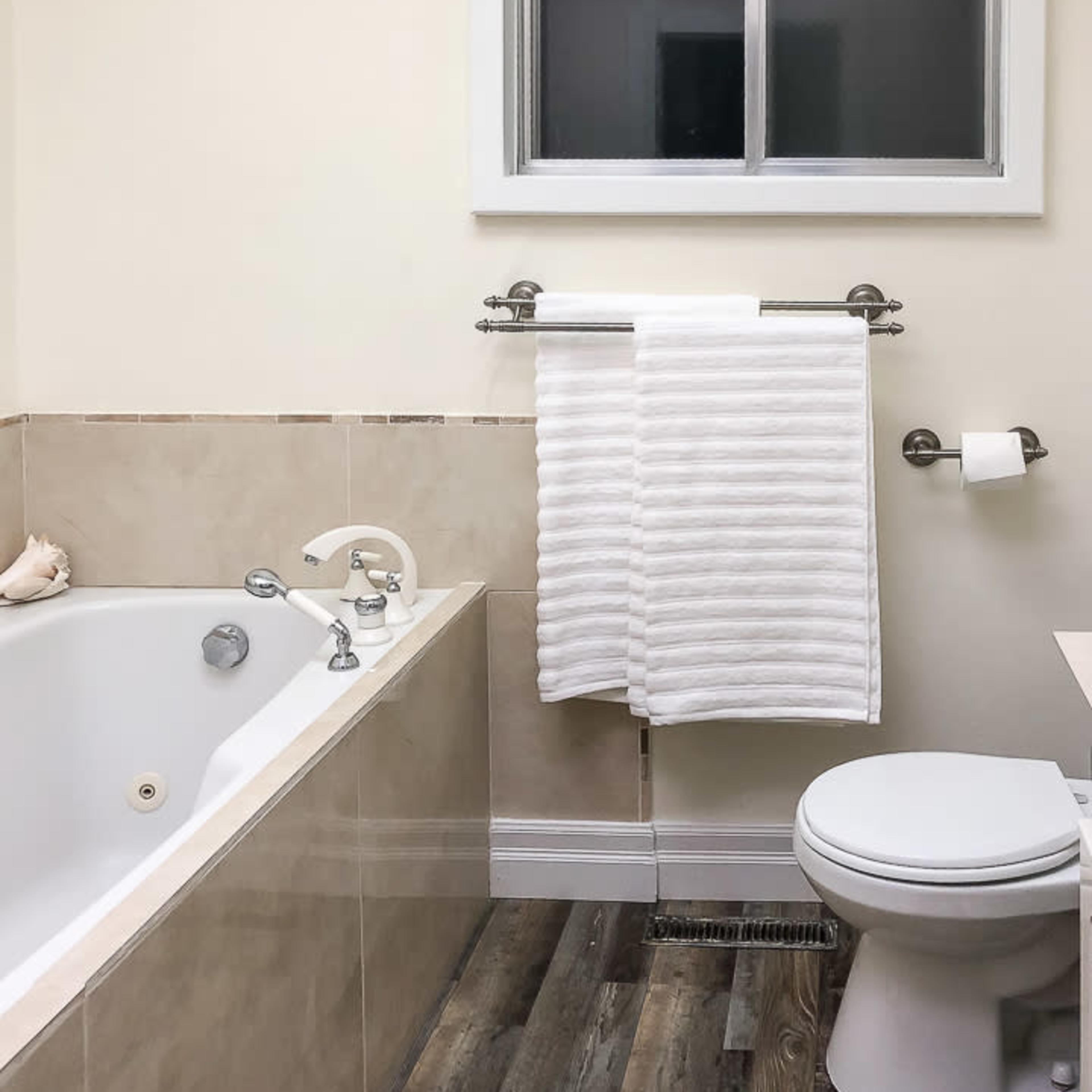 A bathroom featuring a bathtub, a toilet, and a white towel hanging on a rack next to a window.