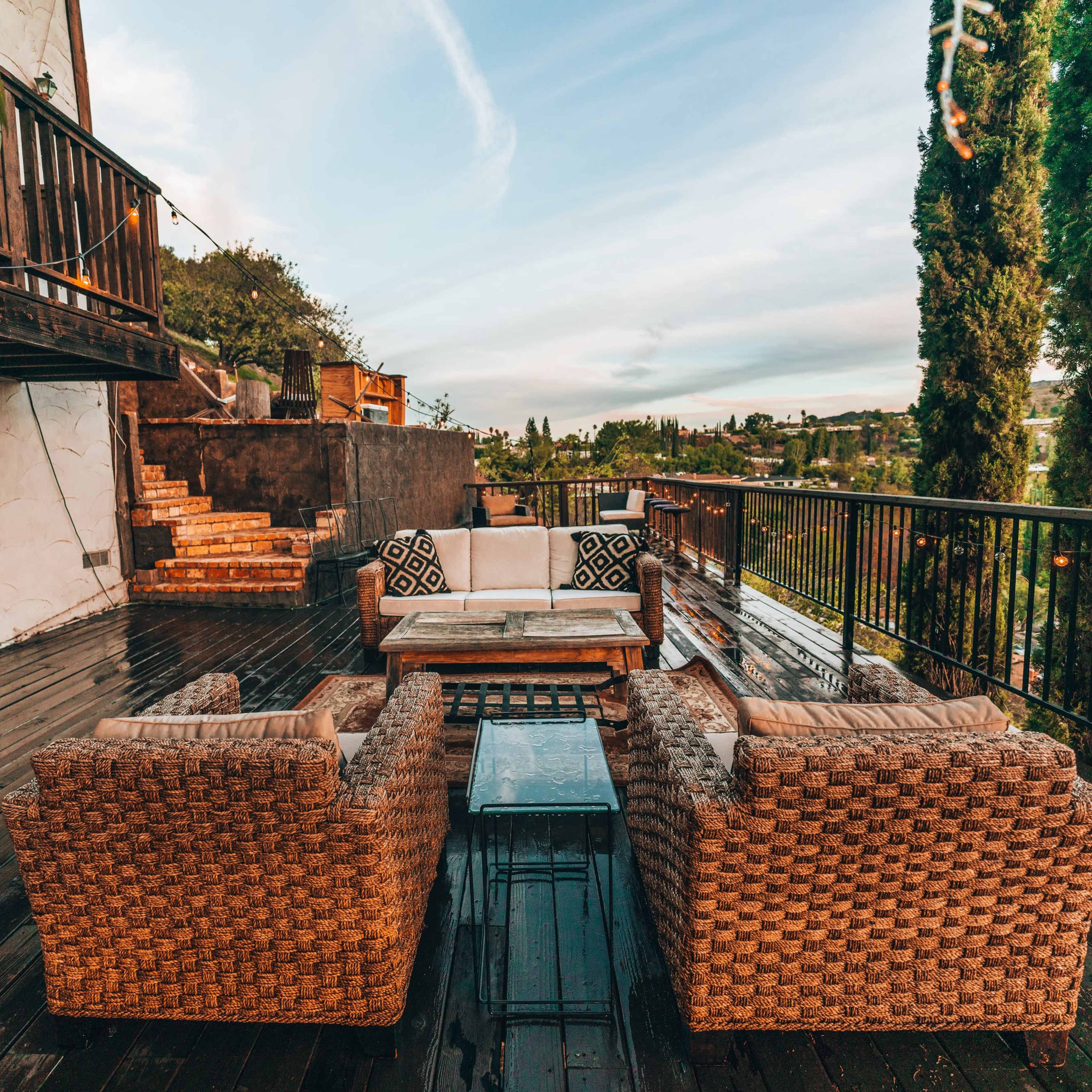 A furnished outdoor deck features a seating area with wicker chairs and a coffee table, overlooking a scenic view.