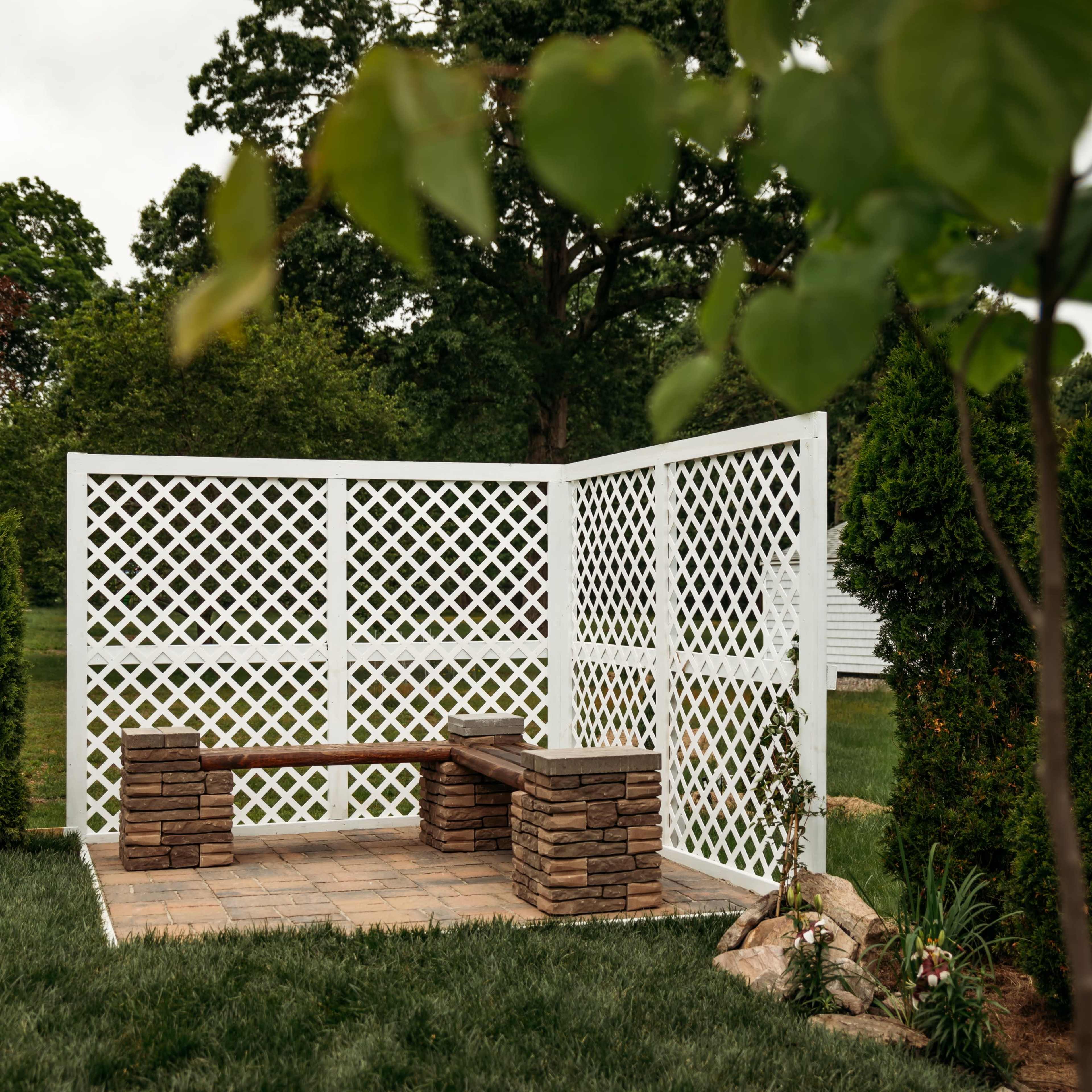 A stone bench sits inside a white lattice privacy screen in a grassy backyard.