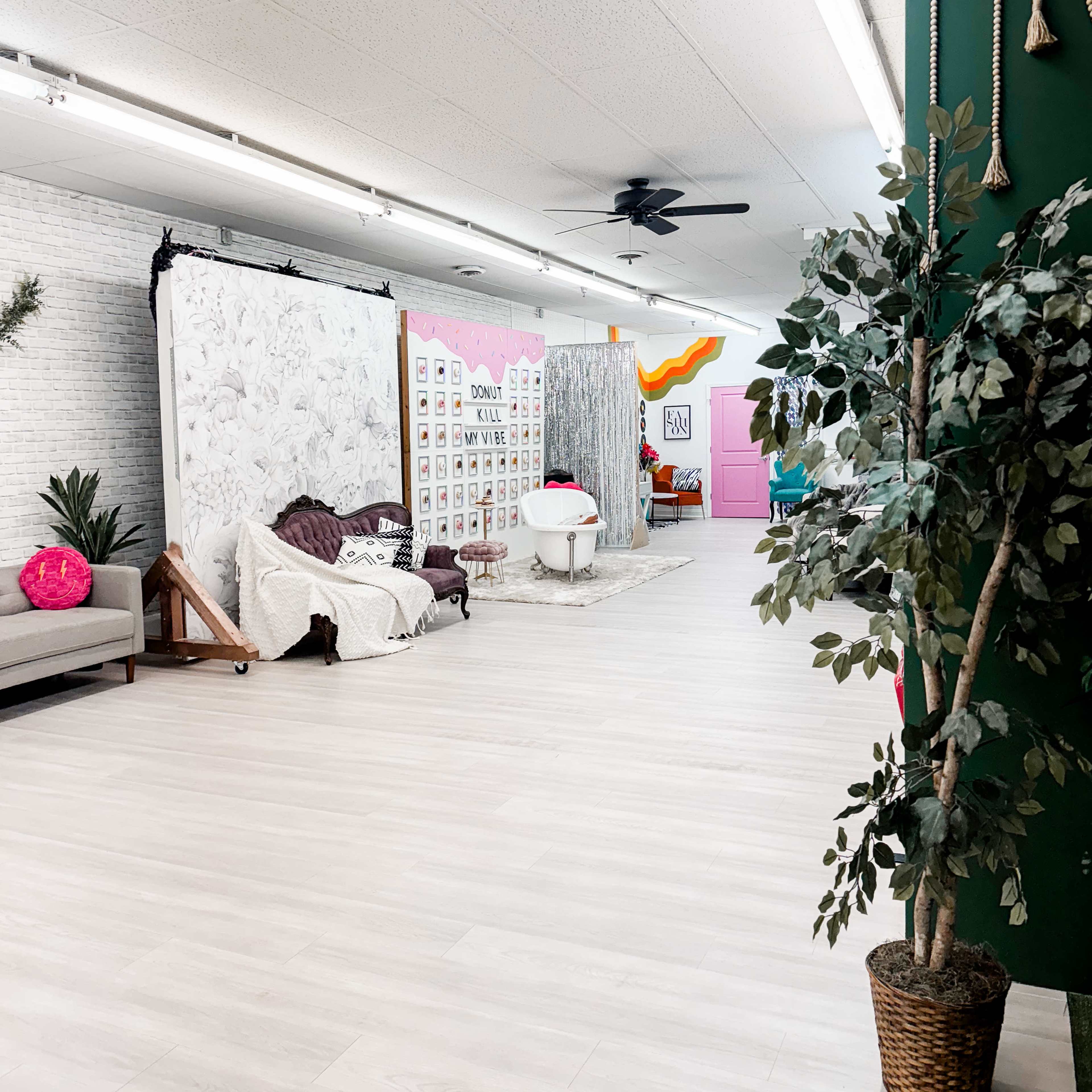 A spacious room with white flooring, featuring a seating area, decorative backgrounds, and plants.