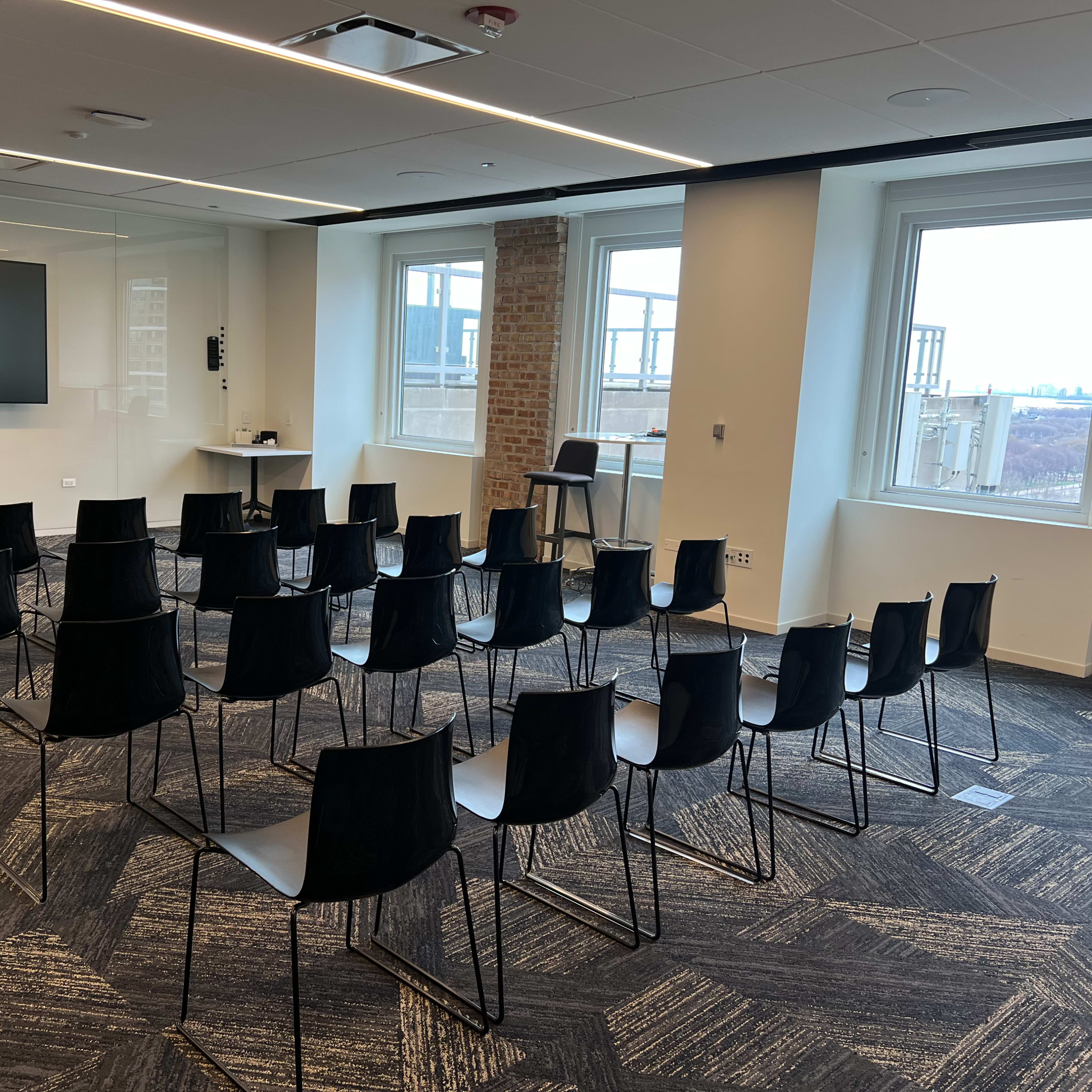 A conference room with a set of black chairs arranged in rows facing a wall-mounted screen.