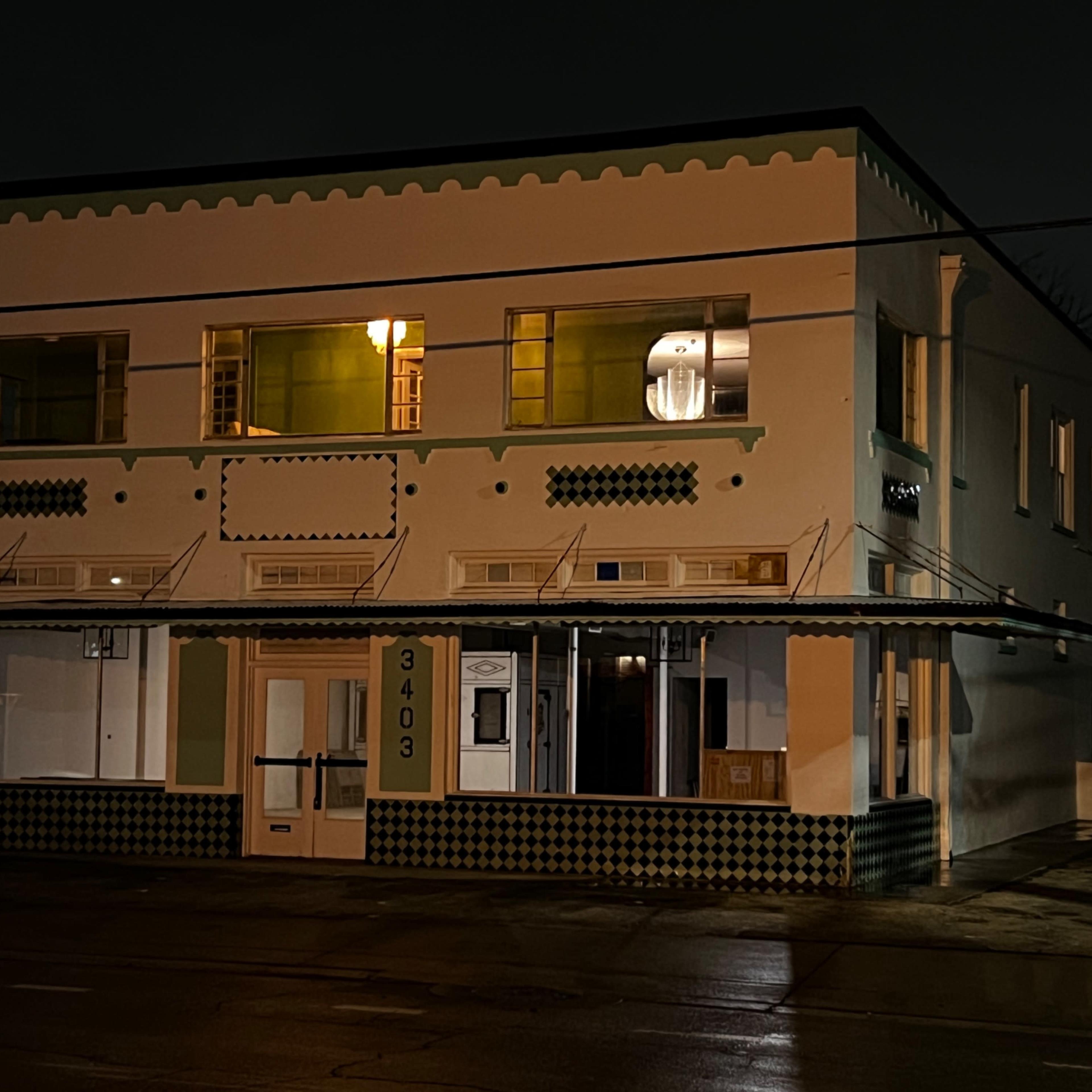 A two-story, brightly lit building with a patterned exterior and storefront on a dark, wet street at night.