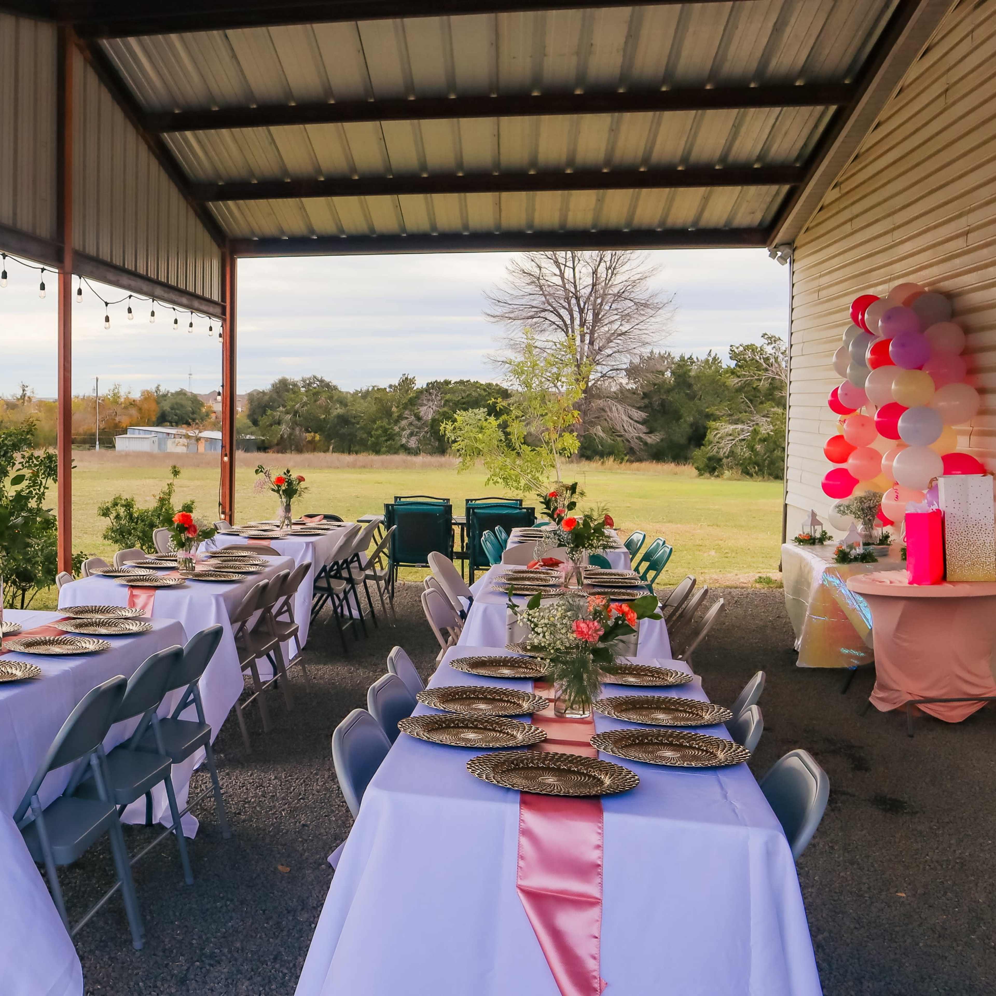 A covered outdoor area features rows of tables set with plates and decorations, alongside a colorful inflatable bounce house.