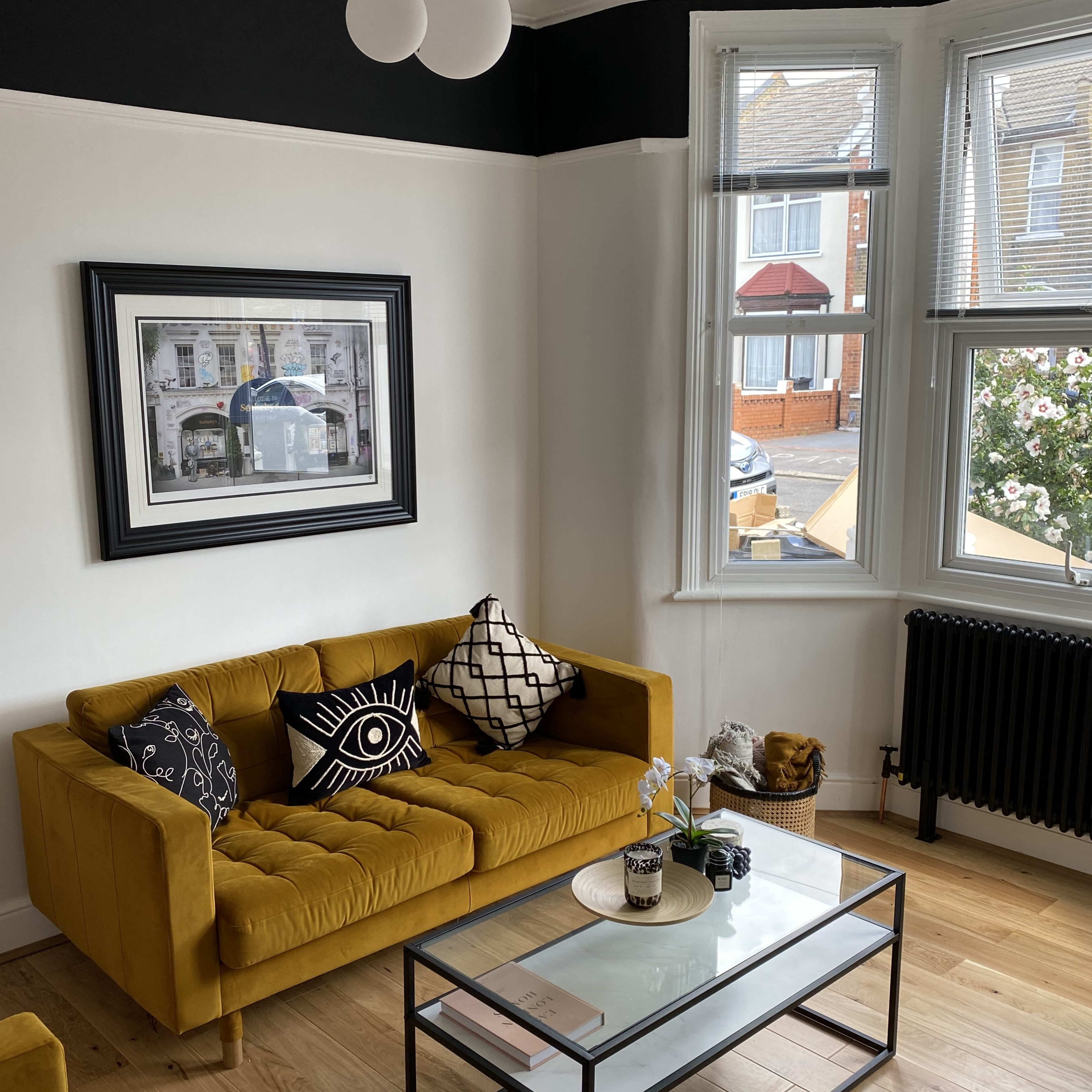 The room features a yellow sofa, a glass coffee table, and a large window with a view of the street outside.