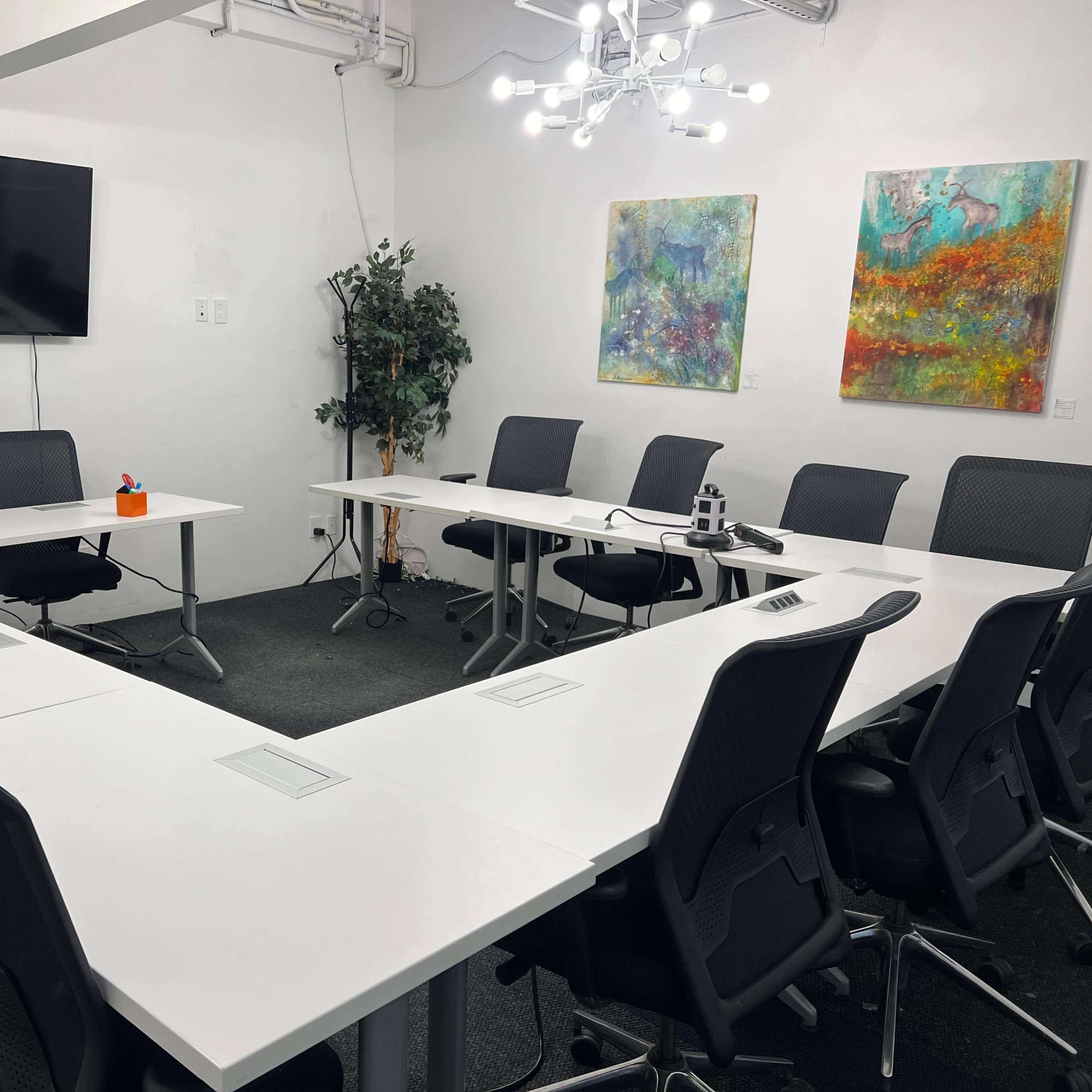 A conference room features a U-shaped table arrangement, a large wall-mounted screen, and two colorful abstract paintings.