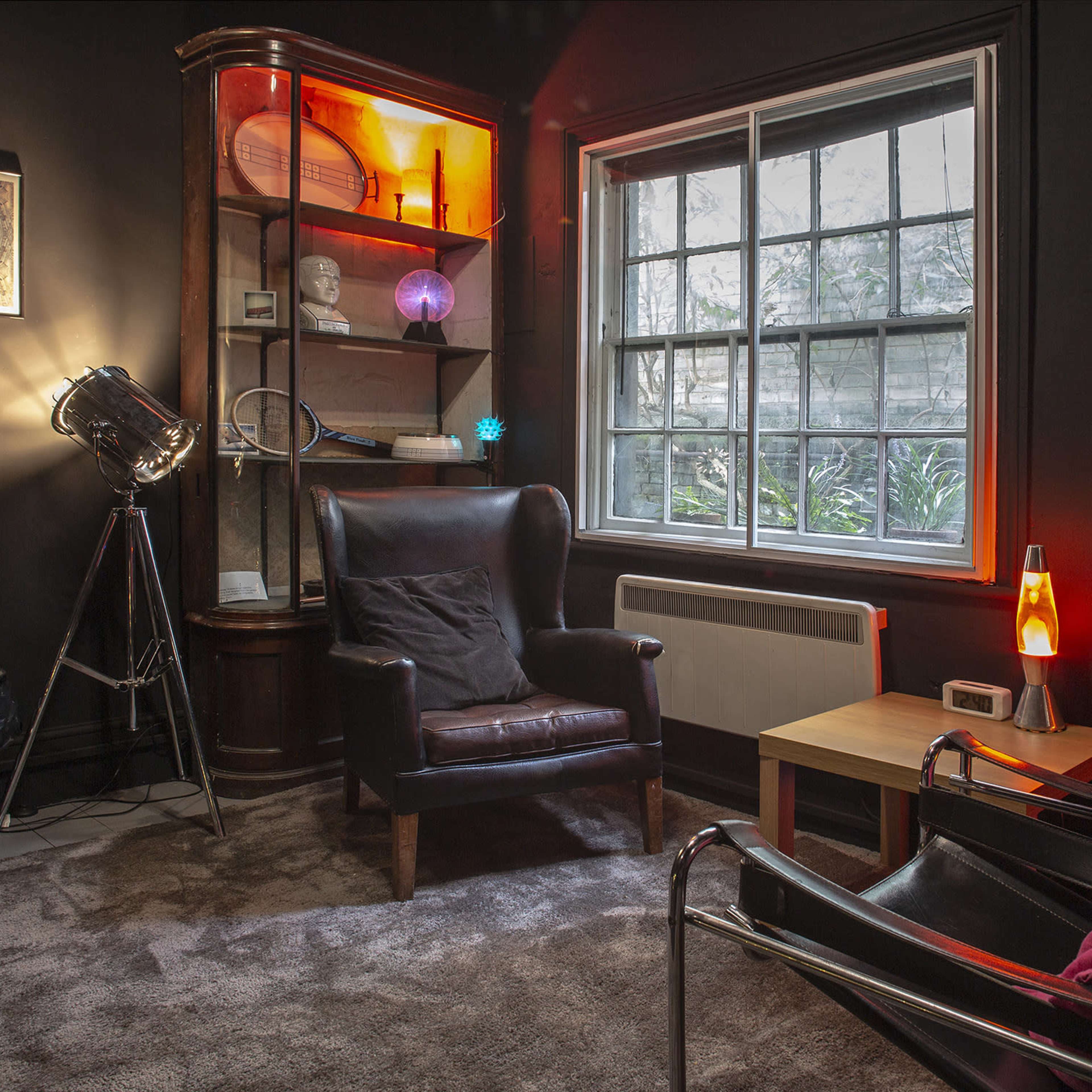 A cozy interior with two chairs, a wooden table, and a window overlooking greenery, illuminated by soft lighting.