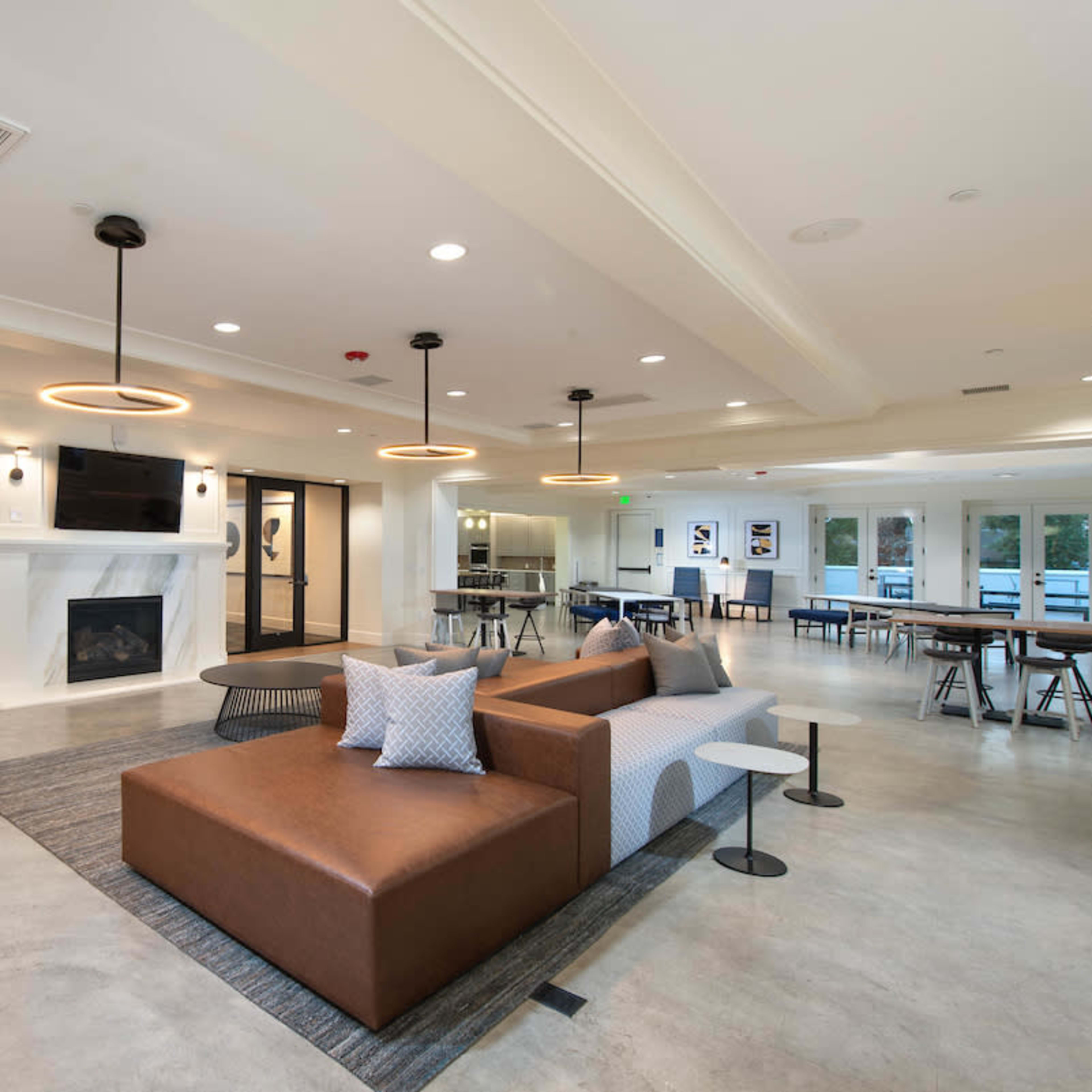 A modern common area featuring a large sectional sofa, a fireplace, and various seating arrangements with tables, all designed for social or collaborative activities.