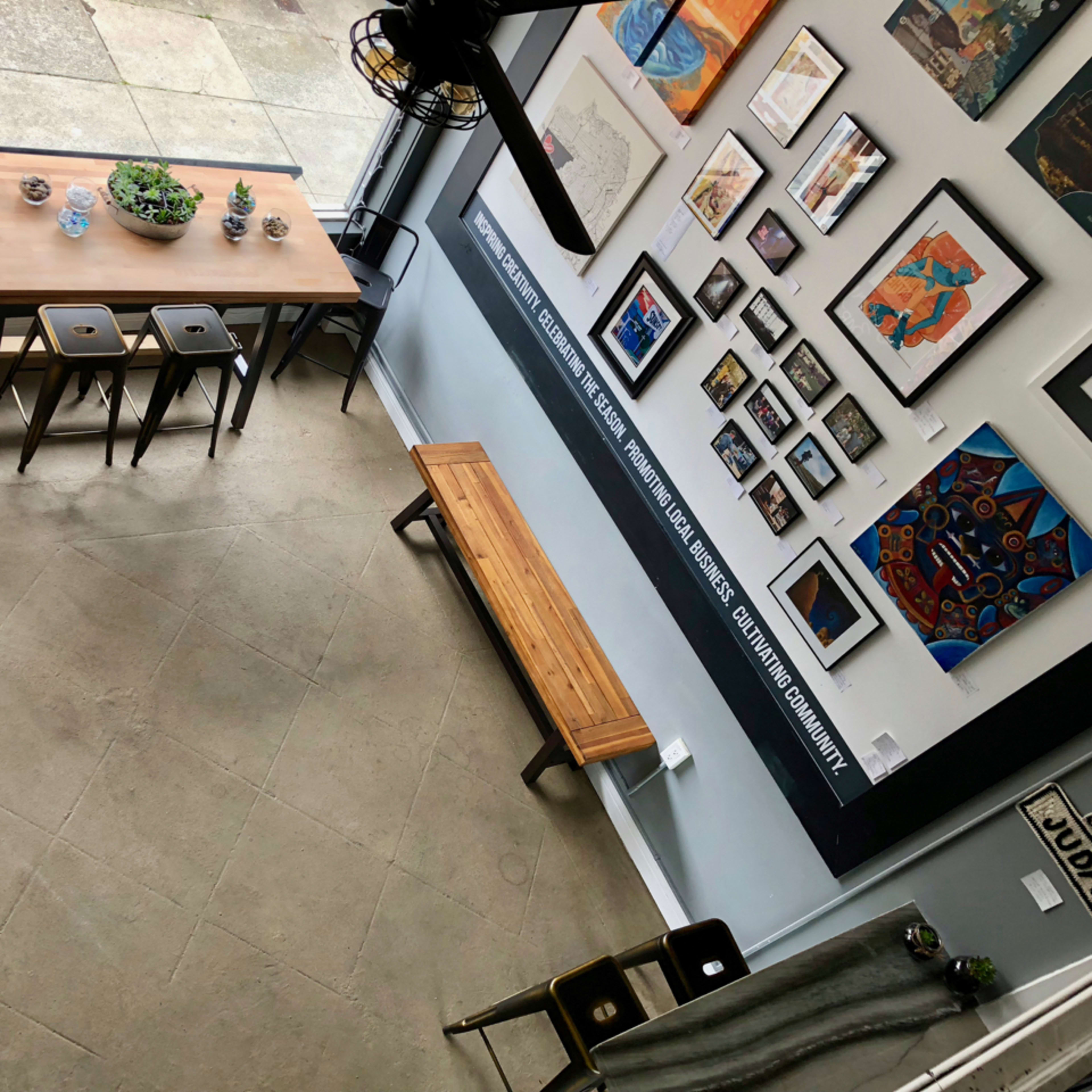 An indoor space featuring a wooden table surrounded by chairs, a bench, and various artworks displayed on the walls.