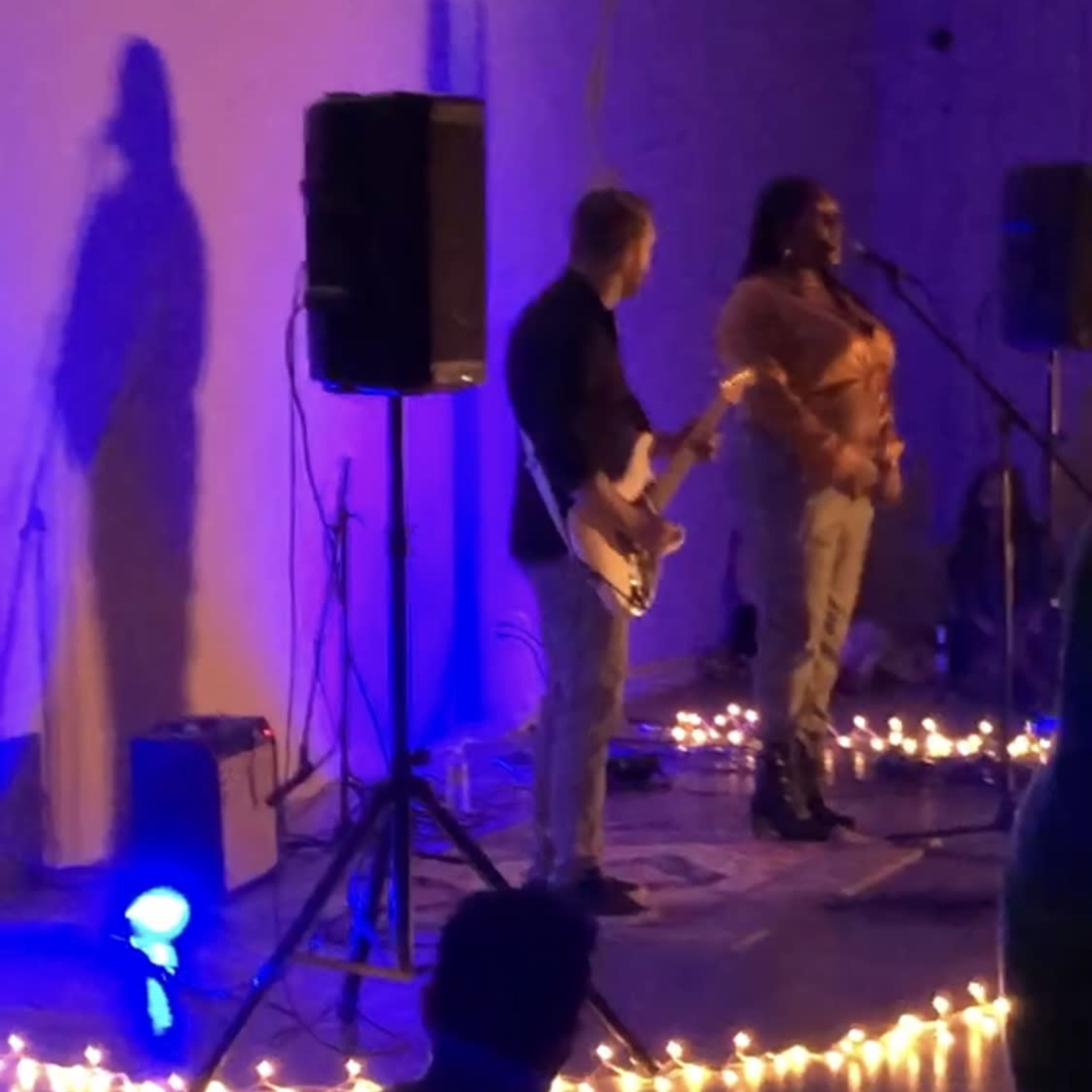 A singer performs on stage while a guitarist accompanies her, illuminated by blue and white lights with a backdrop of soft glowing decorations.