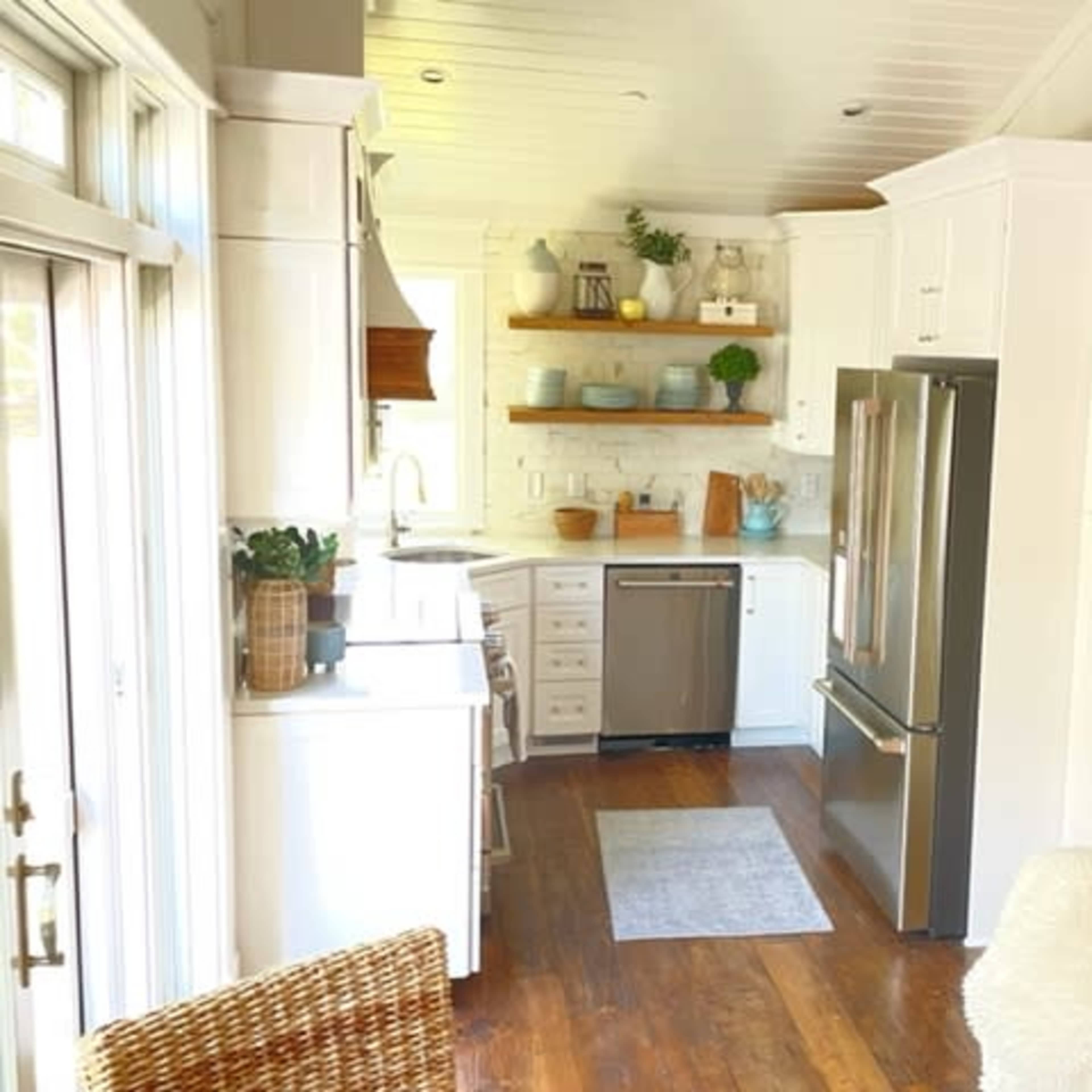 A modern kitchen features white cabinetry, stainless steel appliances, and wooden shelves adorned with various dishes and plants.