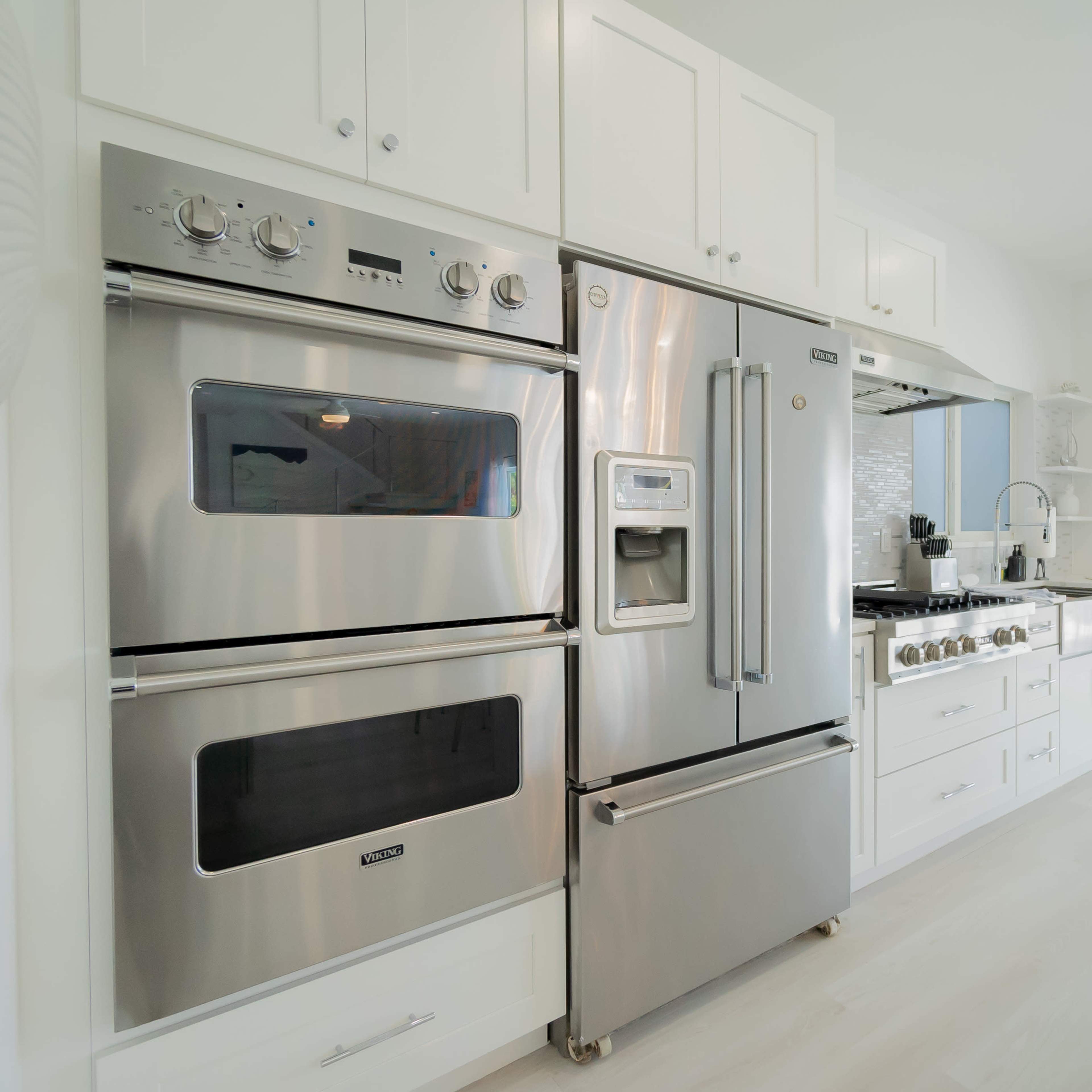 A modern kitchen featuring stainless steel appliances, including an oven, microwave, and refrigerator, with white cabinetry and a view of an outdoor patio.