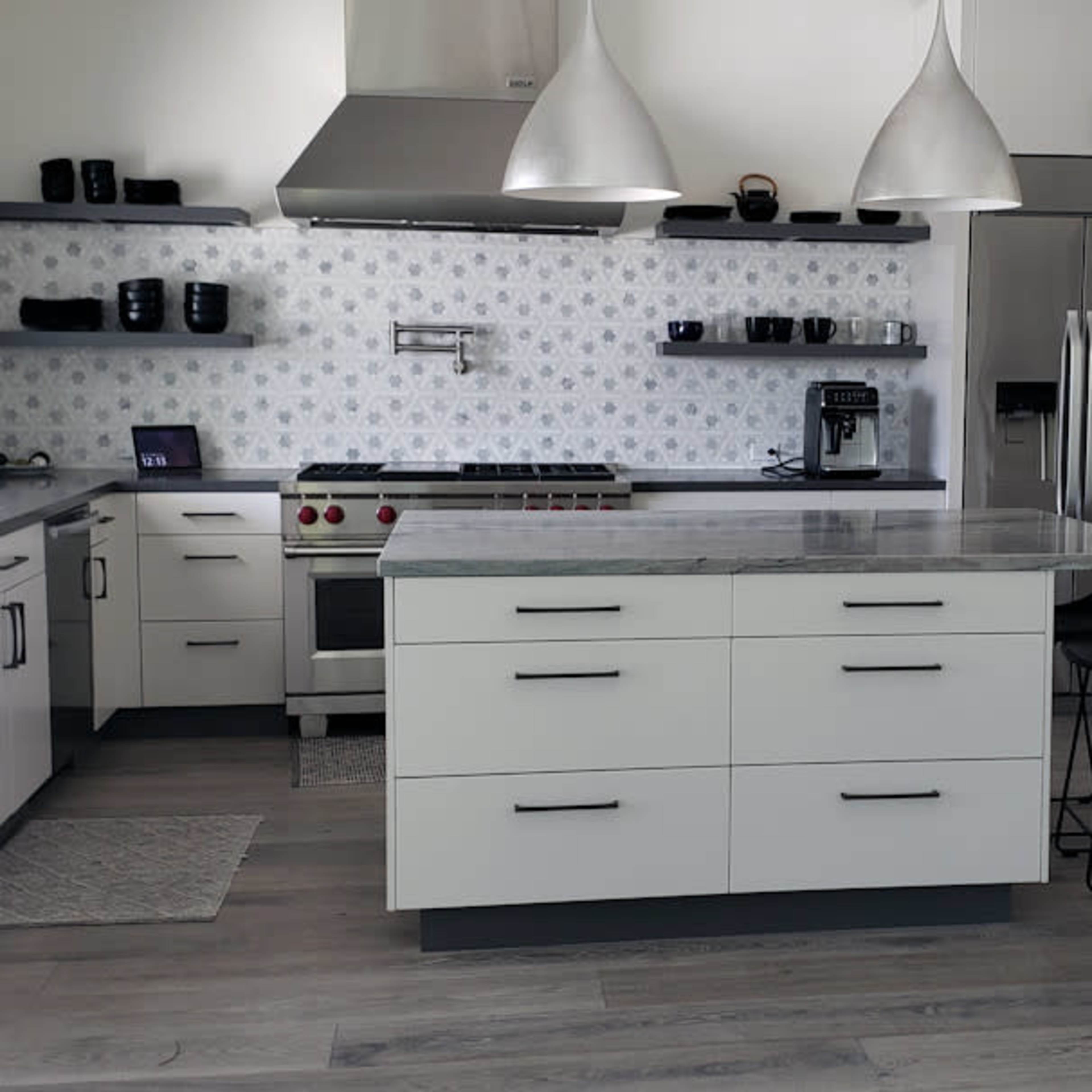 A modern kitchen features a central island, stainless steel appliances, and white cabinetry with gray accents.