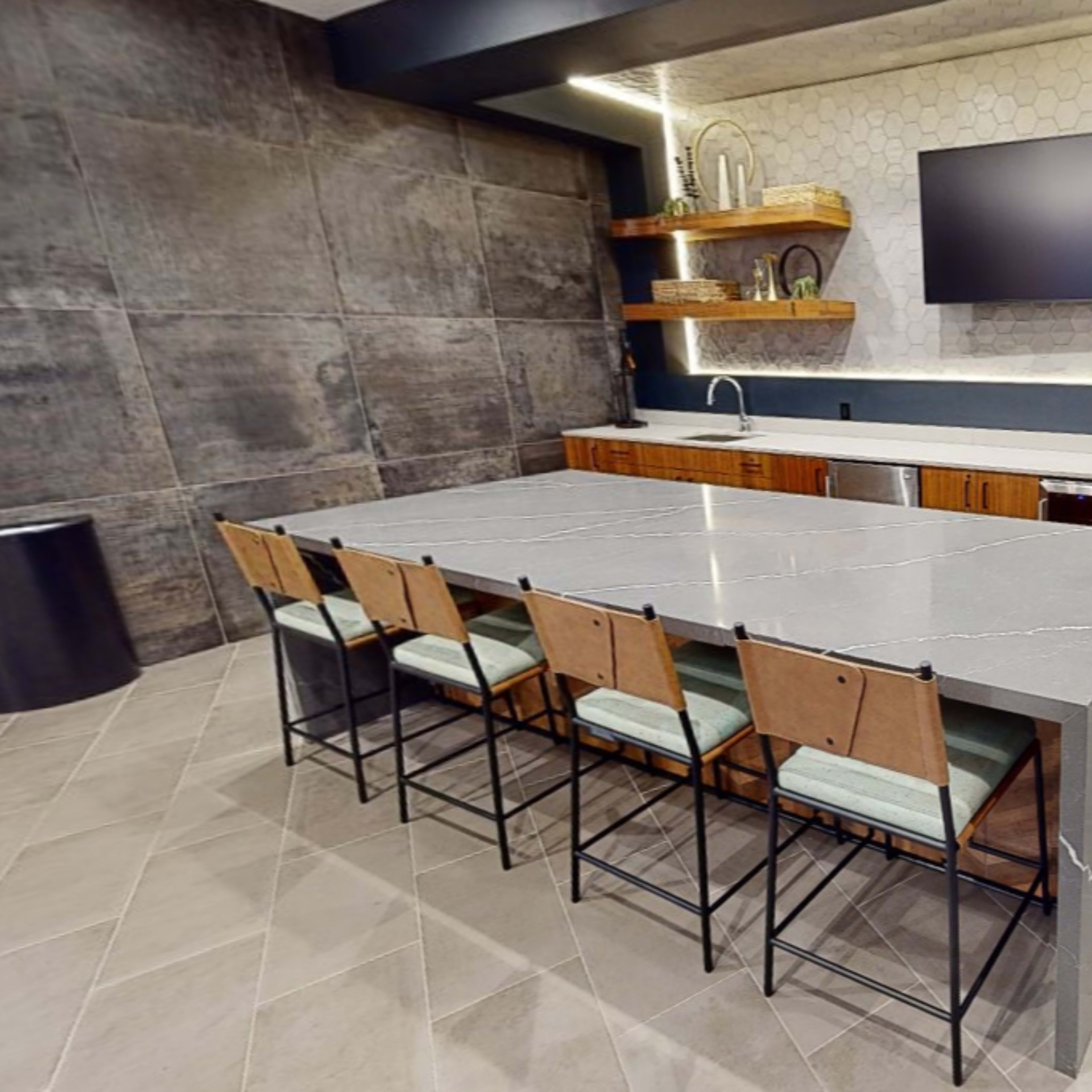 A modern kitchen with a large gray island and wooden cabinets, featuring a wall-mounted television above a countertop.