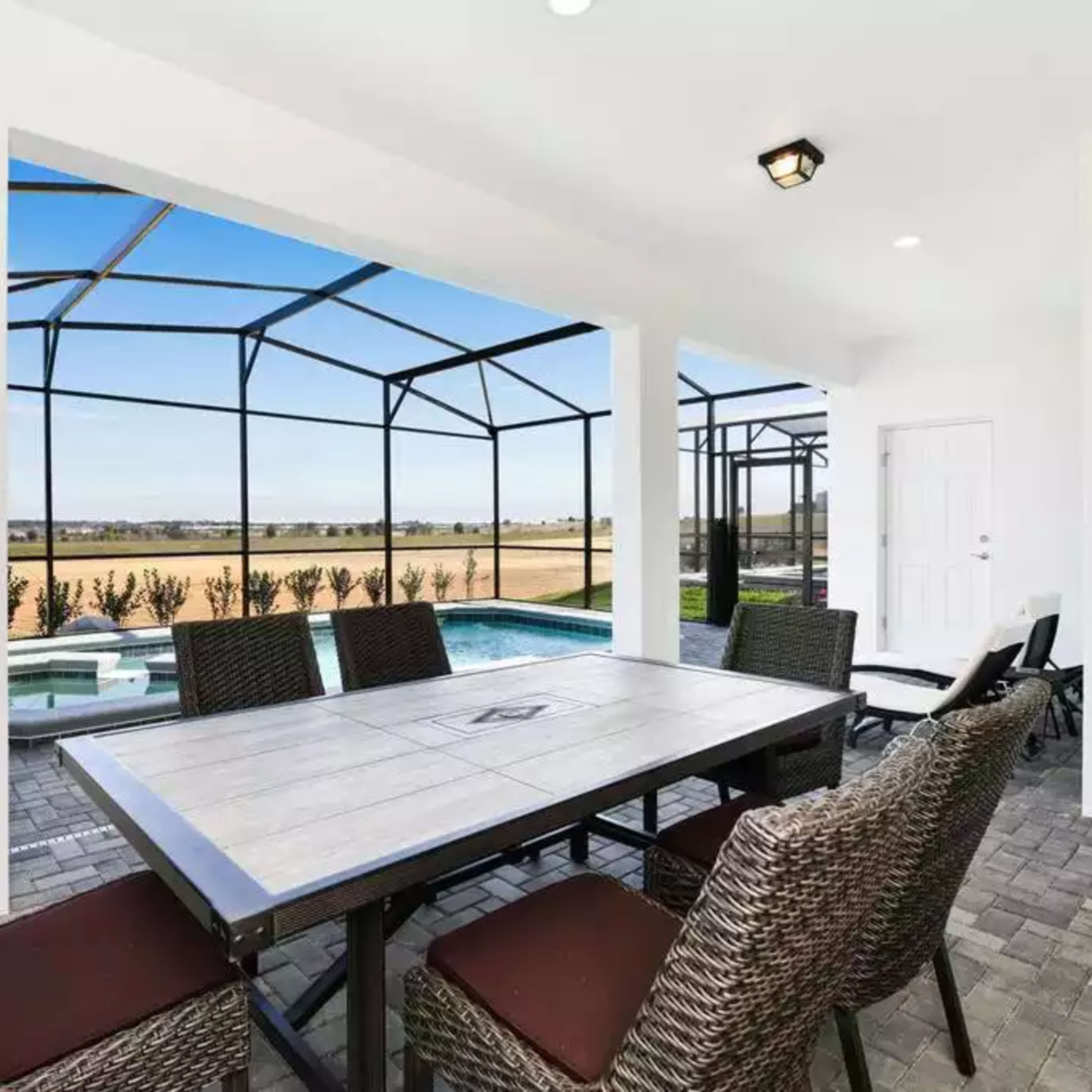 A patio with a table and chairs overlooks a pool area and an open landscape through a screened enclosure.