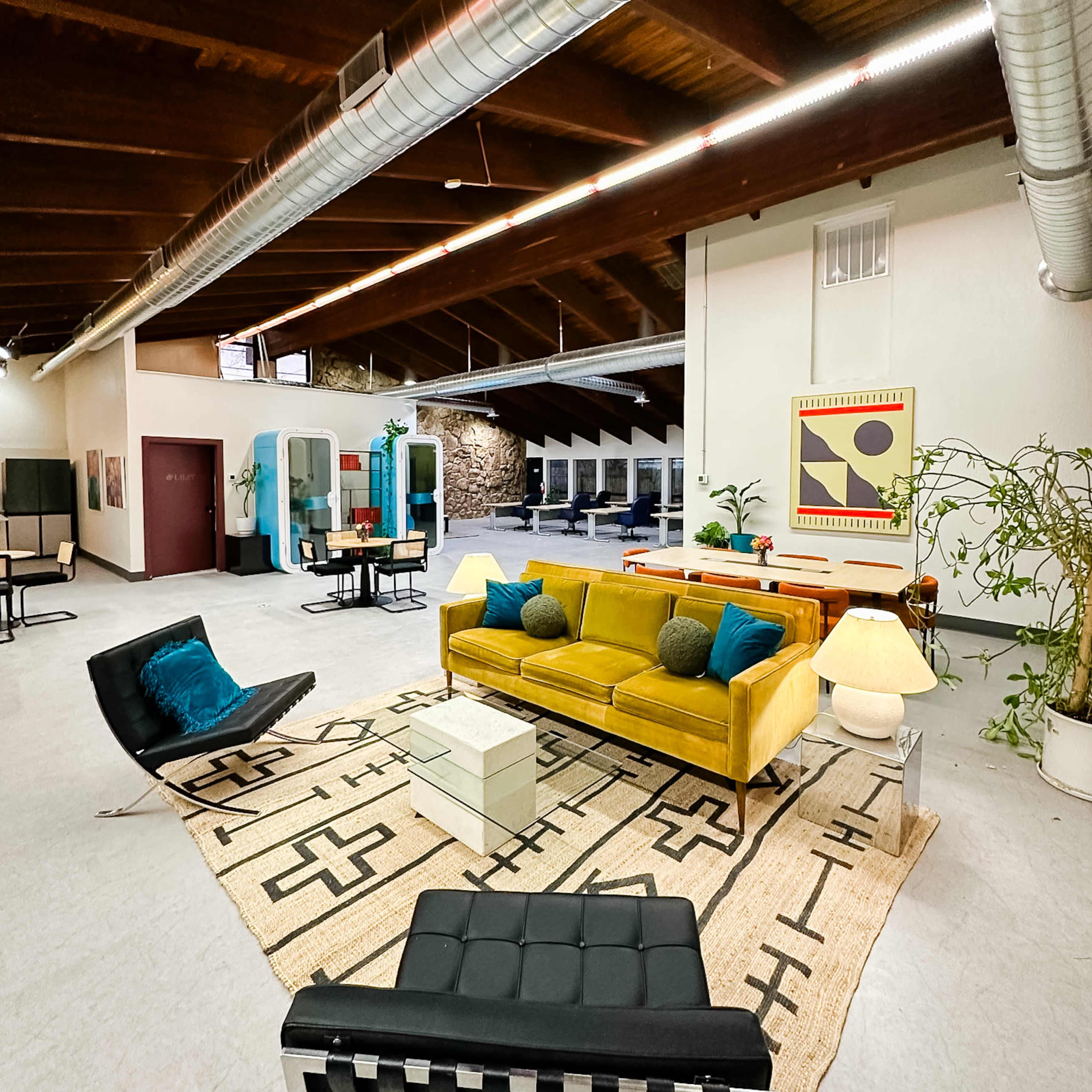 A spacious, modern interior featuring a yellow sofa, a black lounge chair, and various seating areas arranged on a patterned rug.