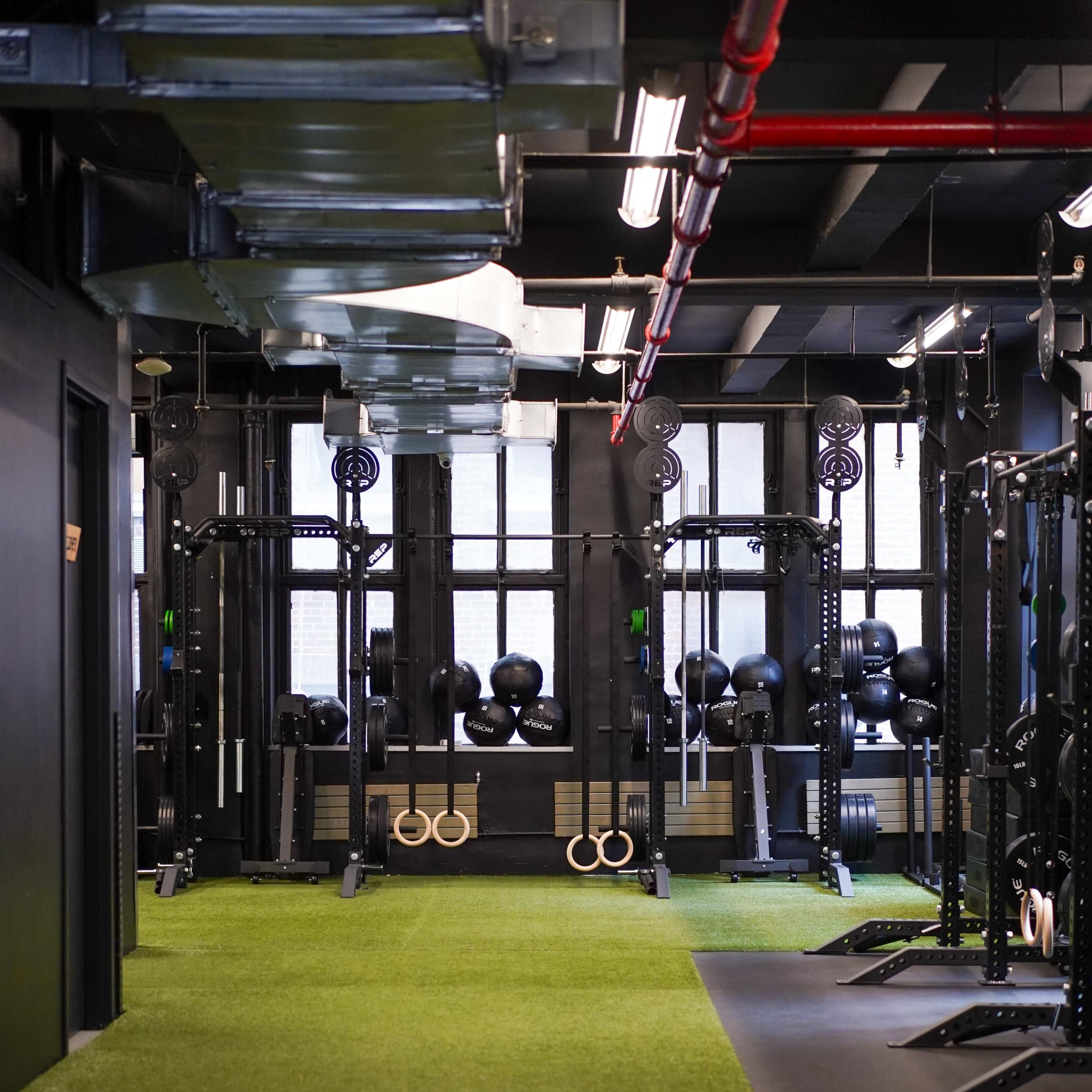 A gym with a turf floor, featuring weightlifting equipment and dumbbells arranged neatly along the walls.