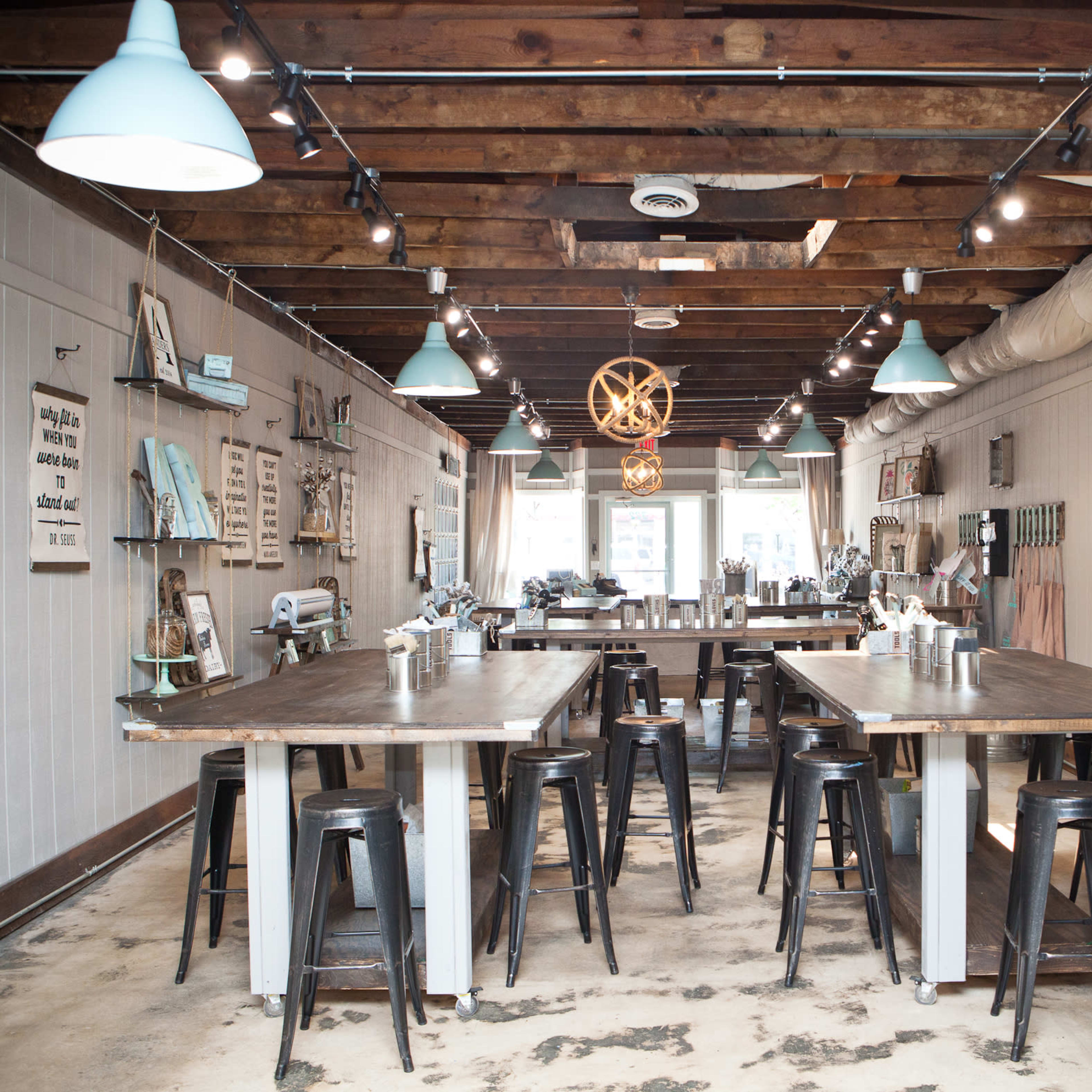 A spacious, well-lit interior of a kitchen workshop with wooden tables, metal stools, and various kitchen tools displayed on the walls.