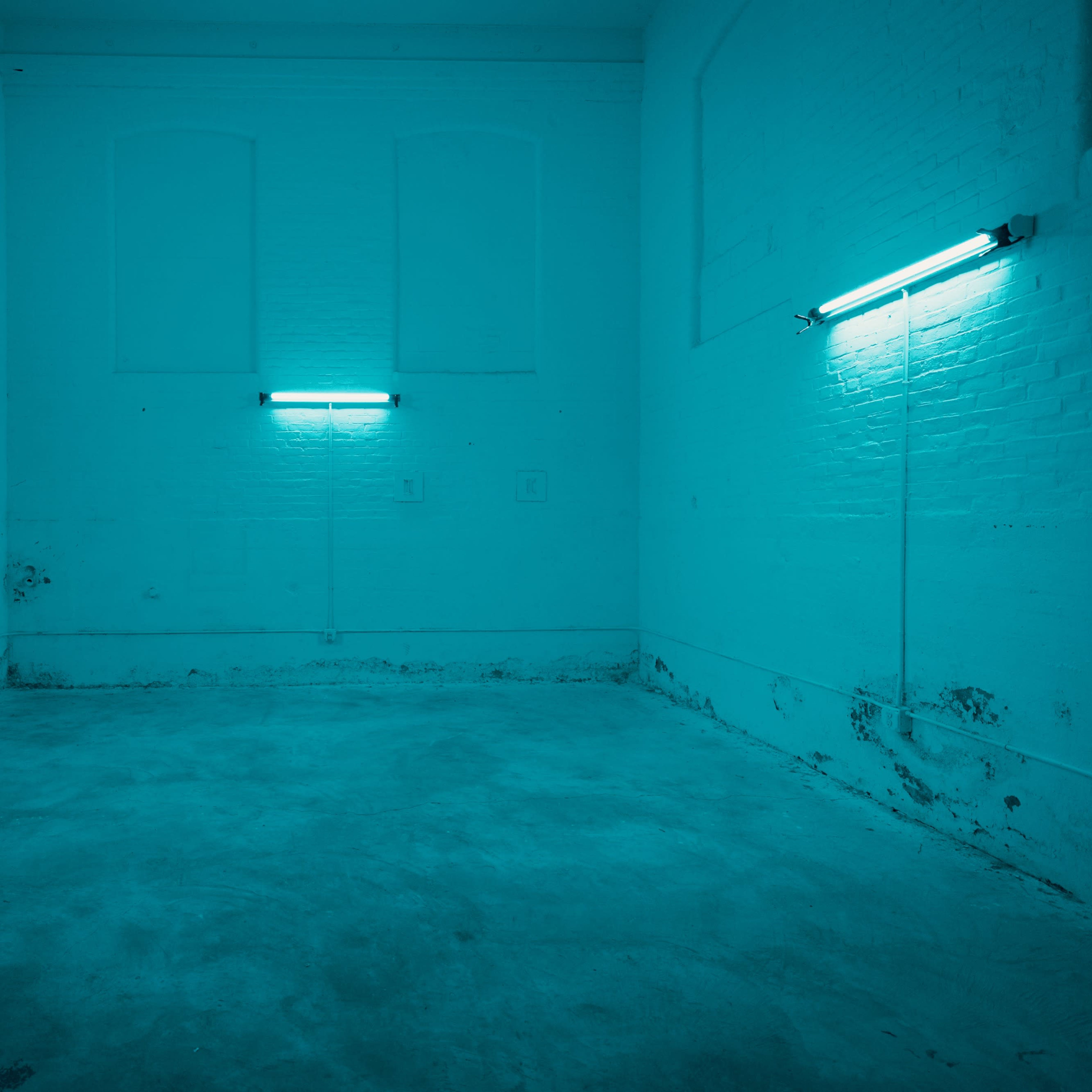 An empty room with turquoise walls and two fluorescent light fixtures mounted on the walls.