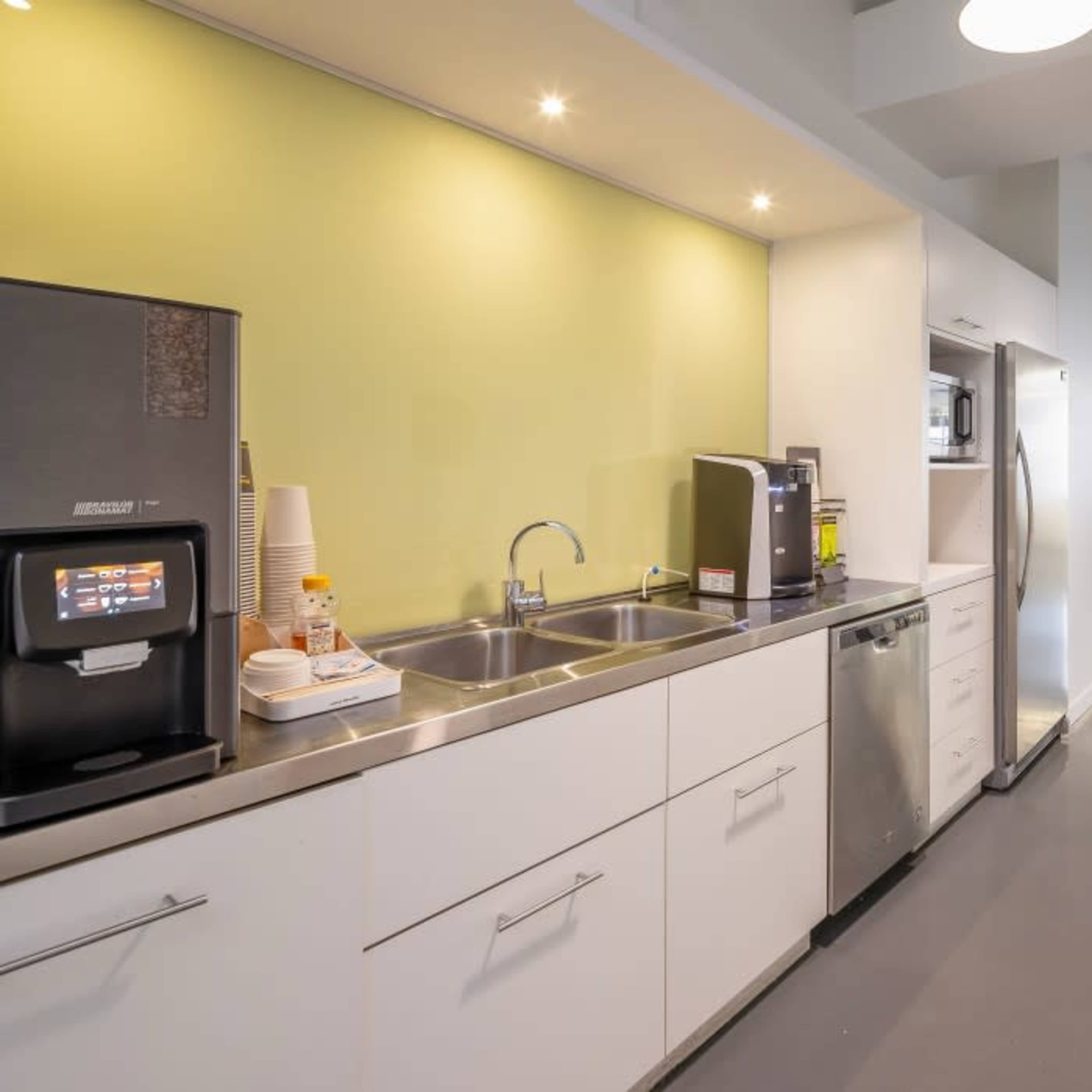 A modern kitchen area with stainless steel appliances, a double sink, and a countertop, featuring a green accent wall and large windows allowing natural light.