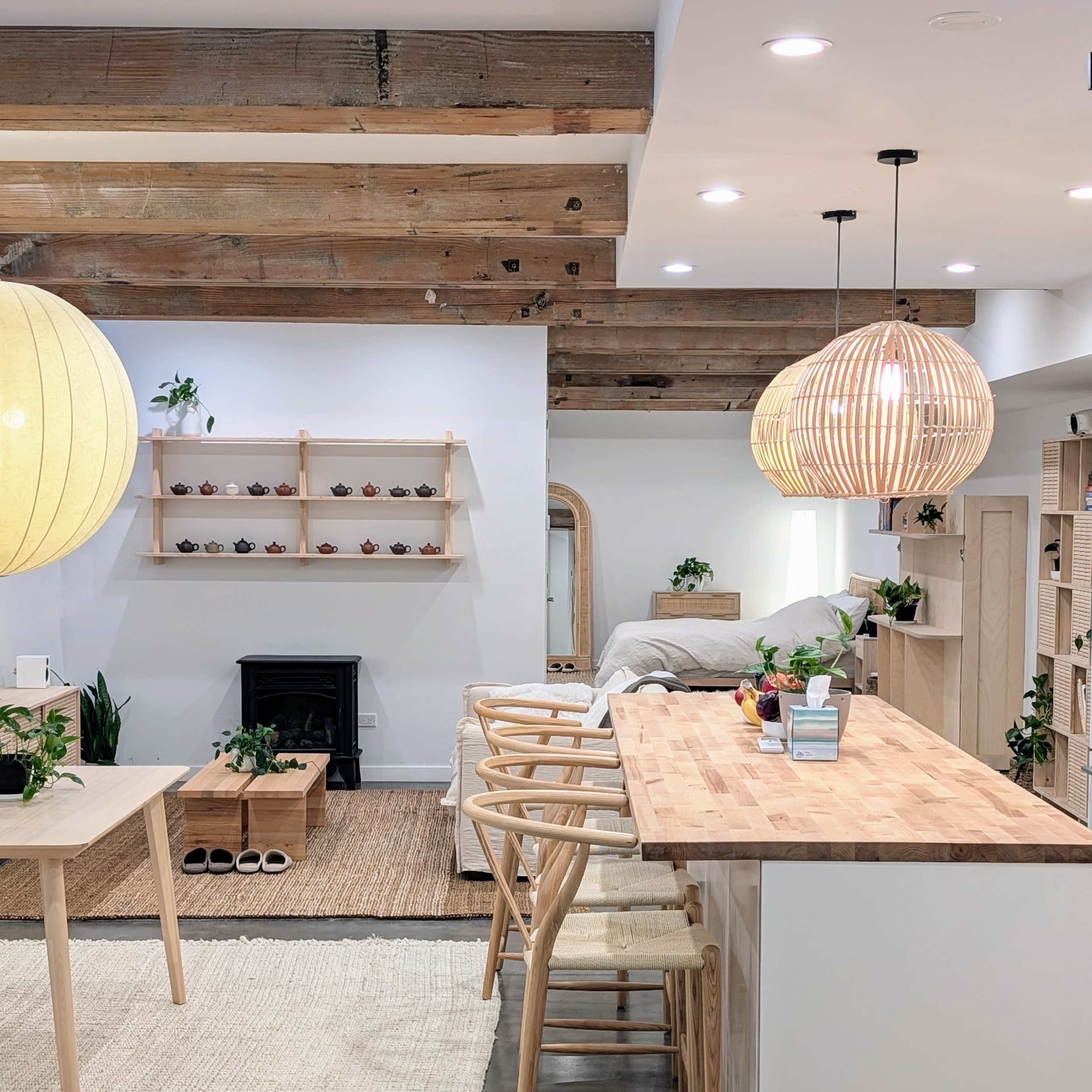 A modern living space with wooden beams, a light-colored kitchen island, bar stools, and various plants arranged throughout.