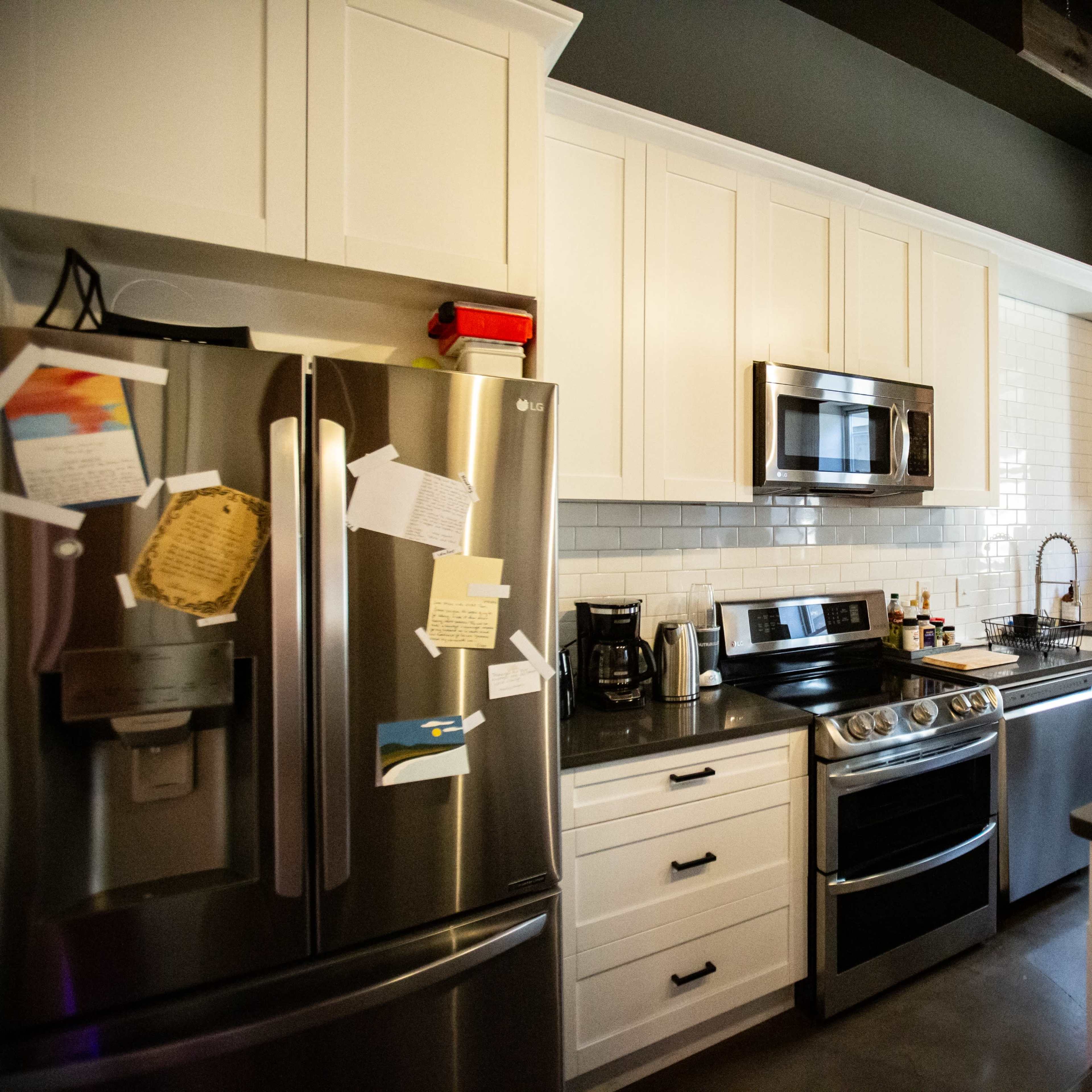 A modern kitchen features stainless steel appliances, white cabinetry, and a dark countertop with a window beside the sink.