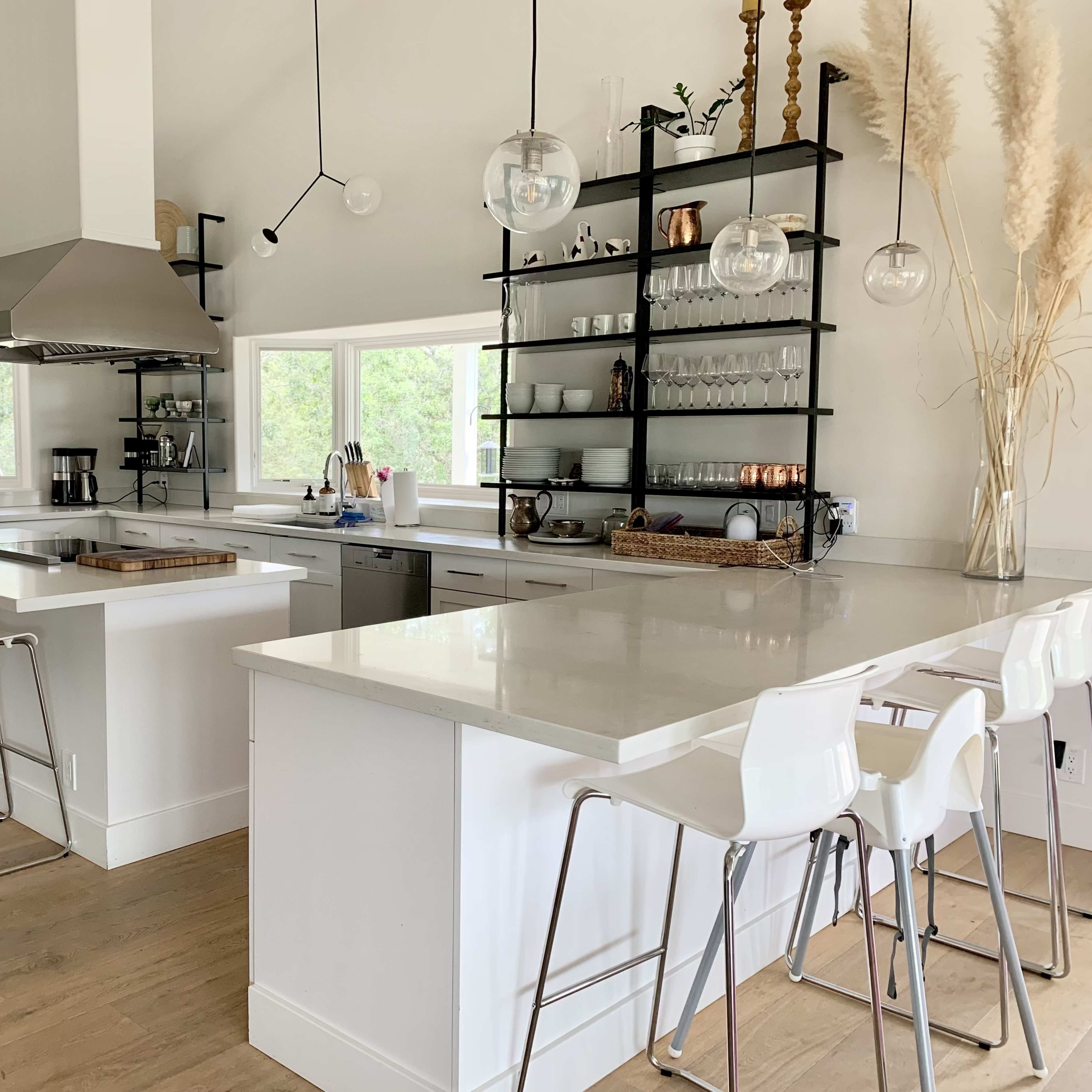 A modern kitchen with white cabinetry, a large island with bar stools, and open shelving displaying glassware.