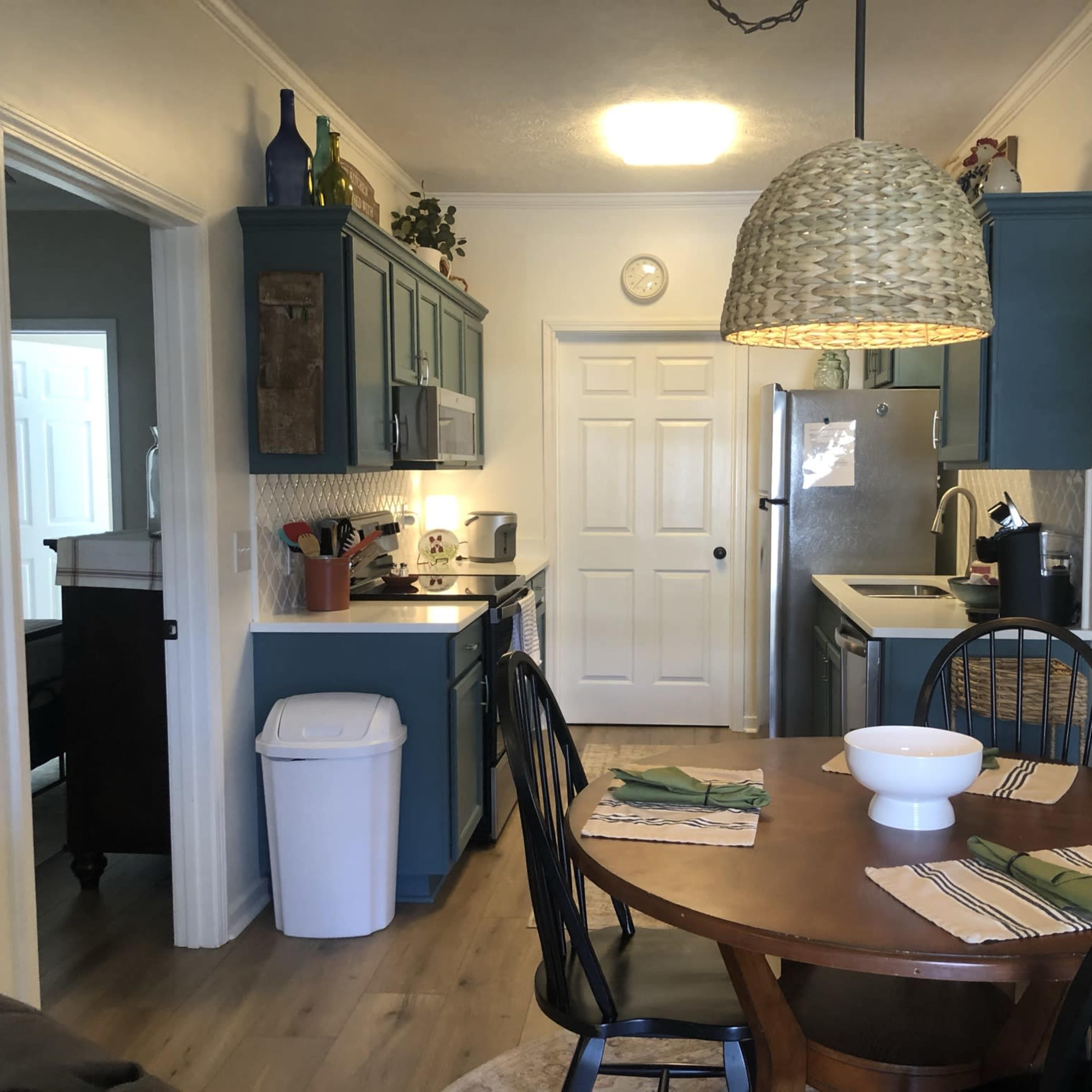 A kitchen and dining area featuring blue cabinets, a round wooden table set for a meal, and an open door leading to another room.