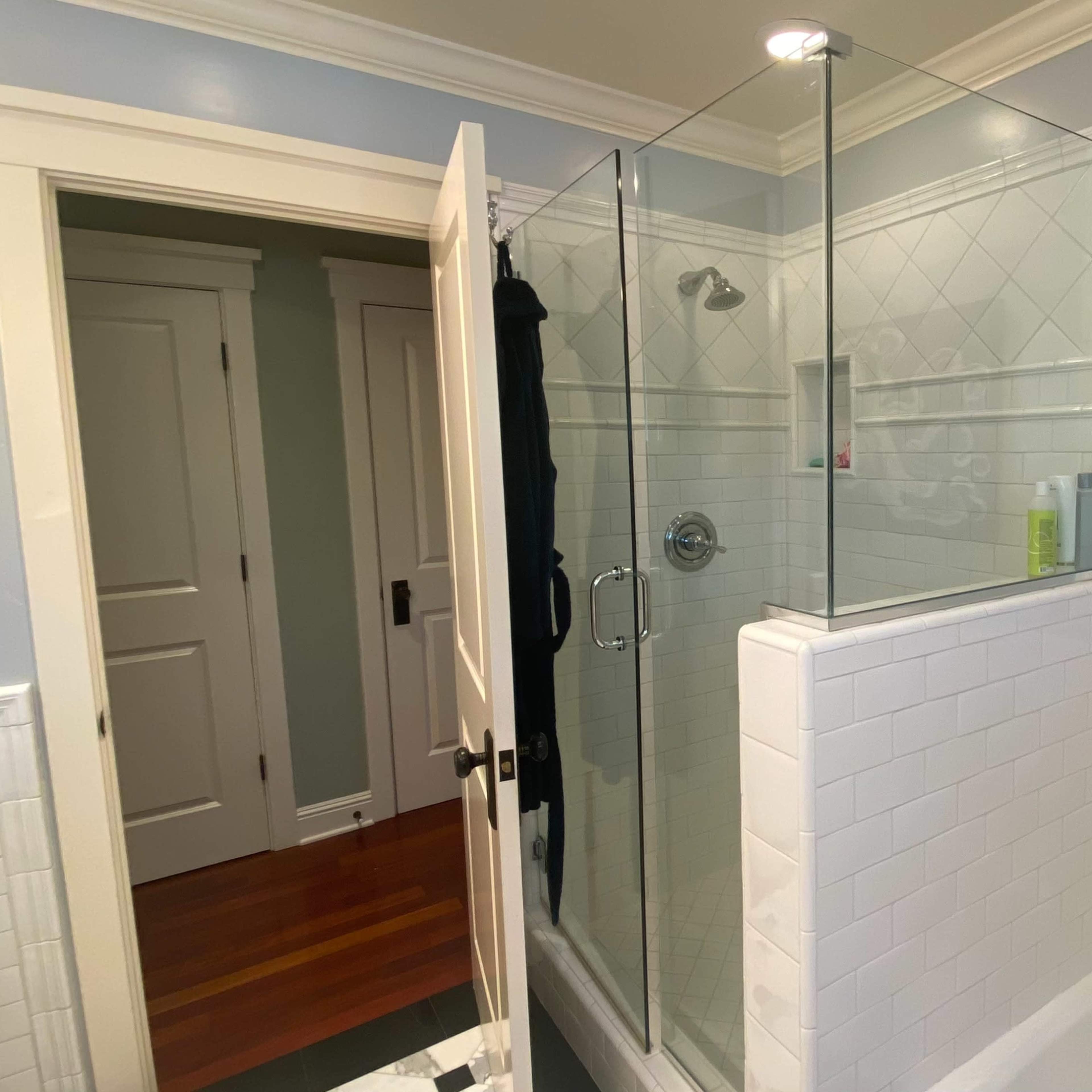 A clean bathroom featuring a glass shower enclosure, white tiled walls, and a dark blue artwork depicting an octopus.