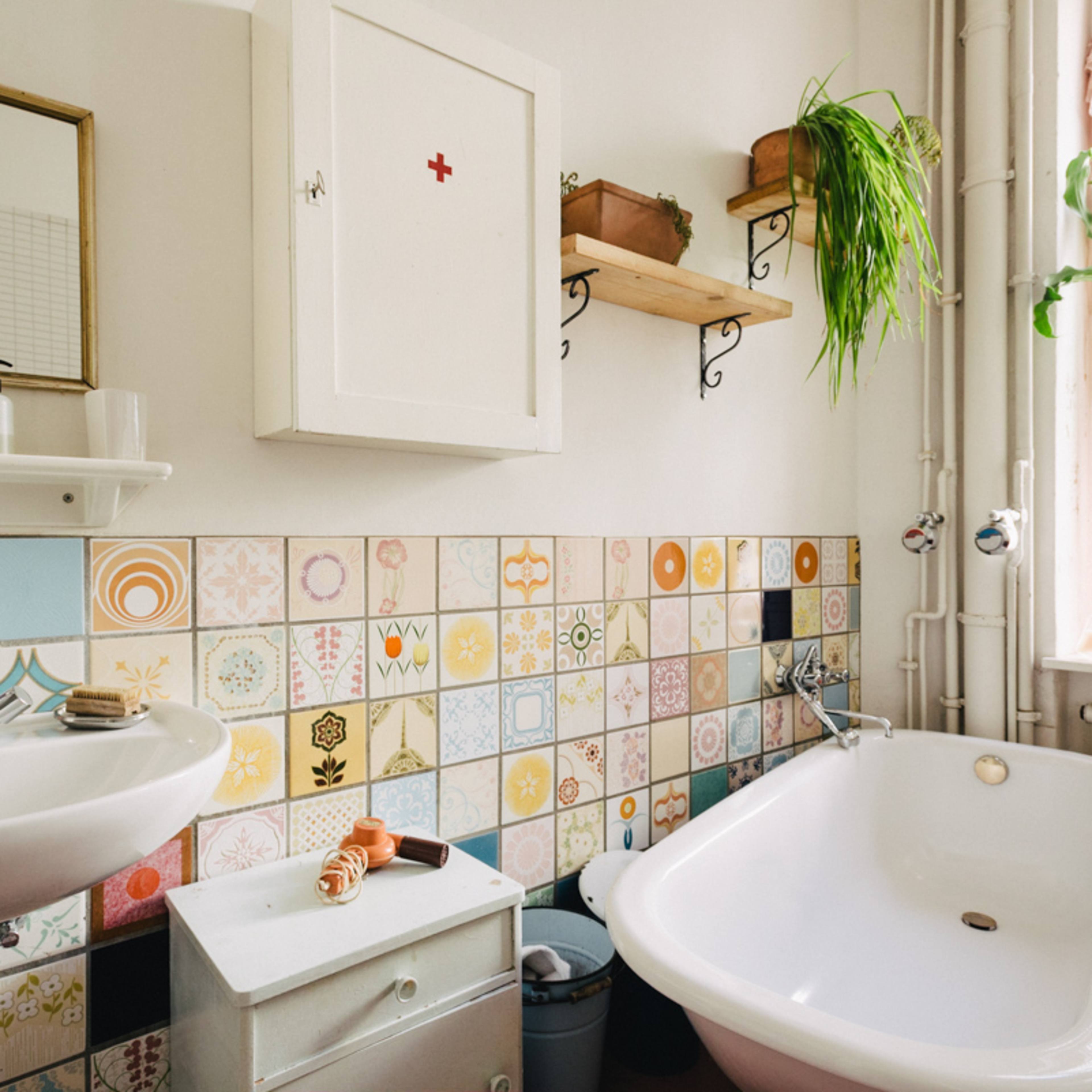 A bathroom featuring a white bathtub, a sink with toiletries, and a colorful tiled wall with floral patterns.