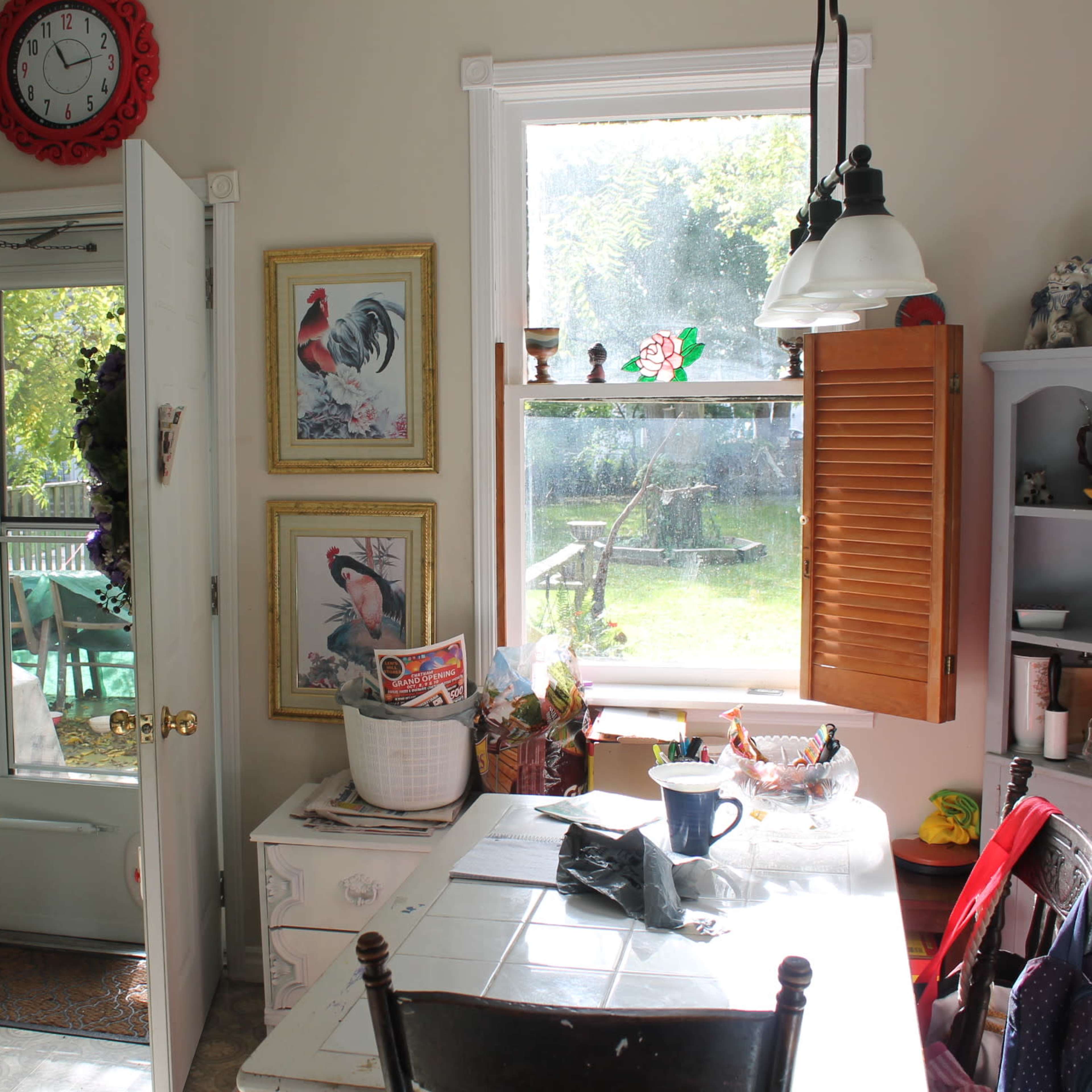 A kitchen with a door leading to an outdoor space, featuring a table, chairs, and framed pictures on the walls, illuminated by natural light.