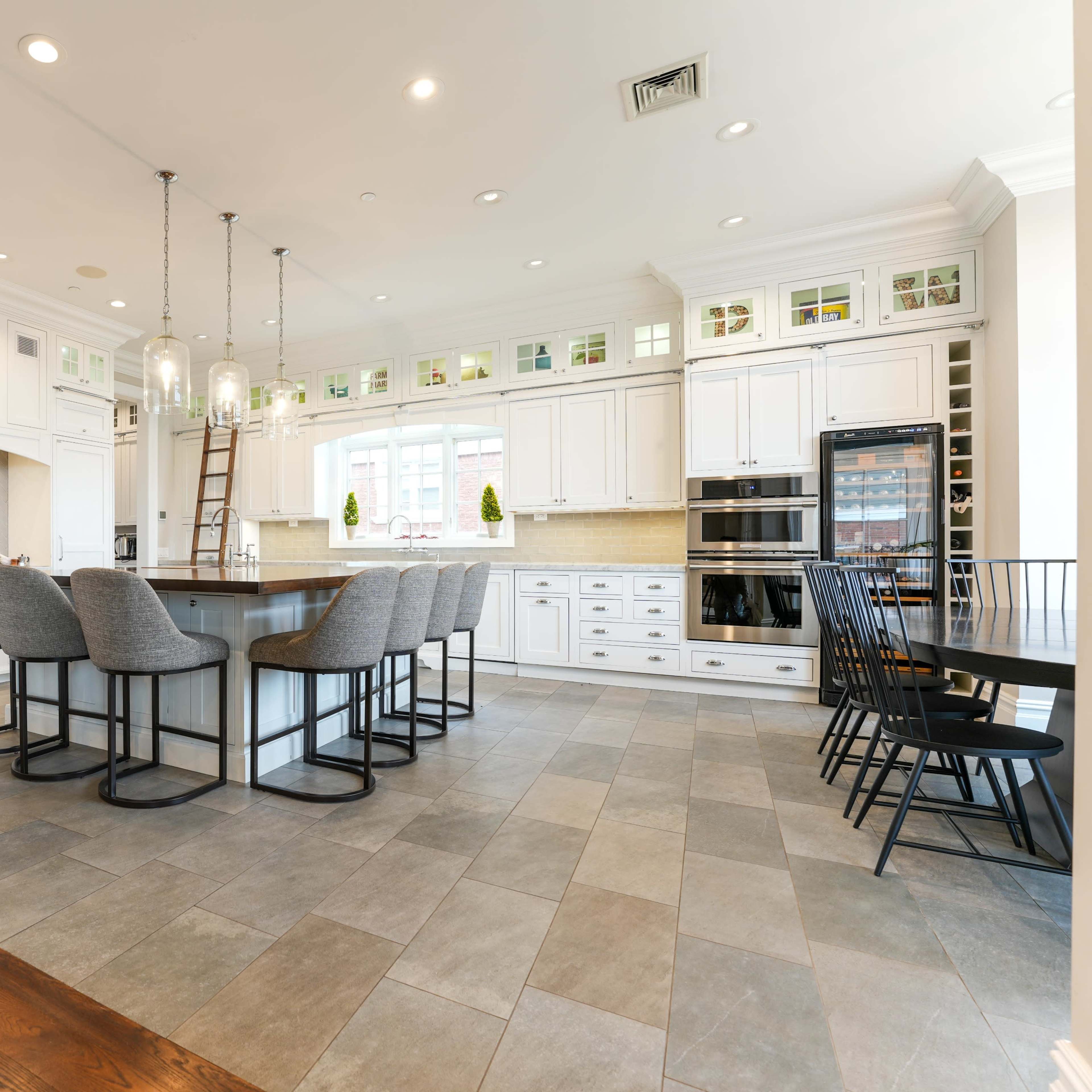 A modern kitchen with an island, bar seating, and white cabinetry, featuring large windows that illuminate the space.
