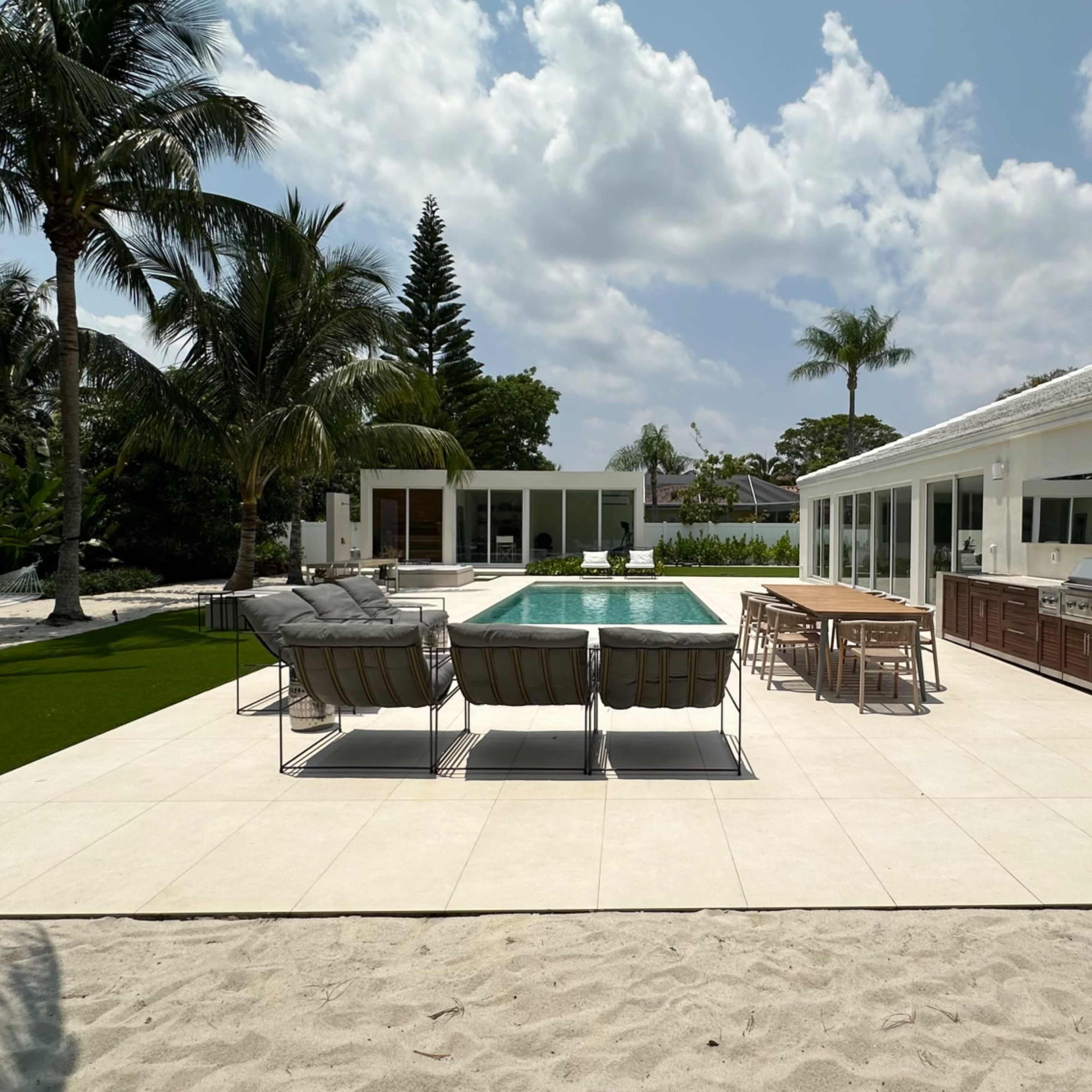 A modern outdoor space with a swimming pool, lounge chairs, a dining area, and tropical landscaping.