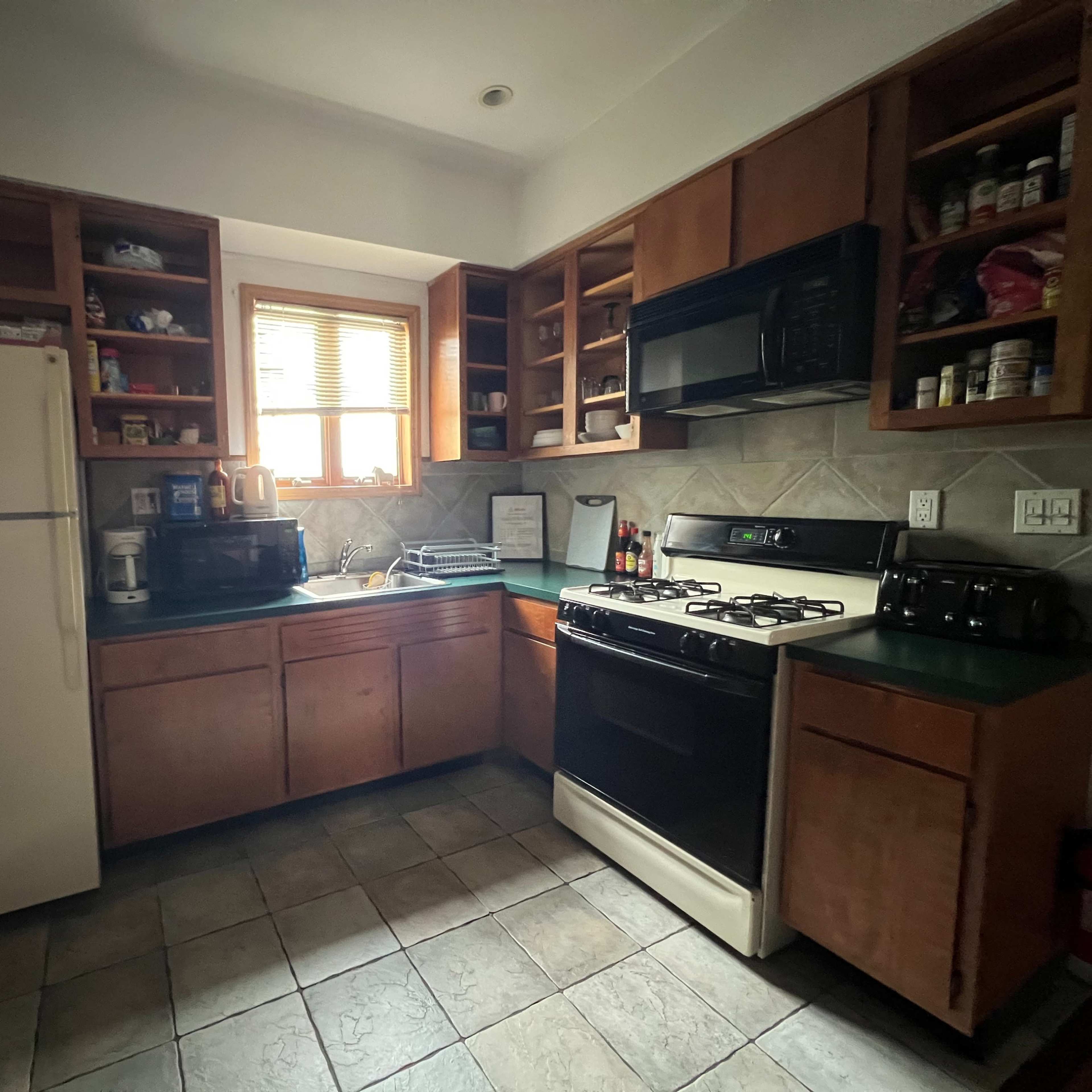 A kitchen with wooden cabinets, a stove, a microwave, and a refrigerator, featuring a window that allows light to enter.