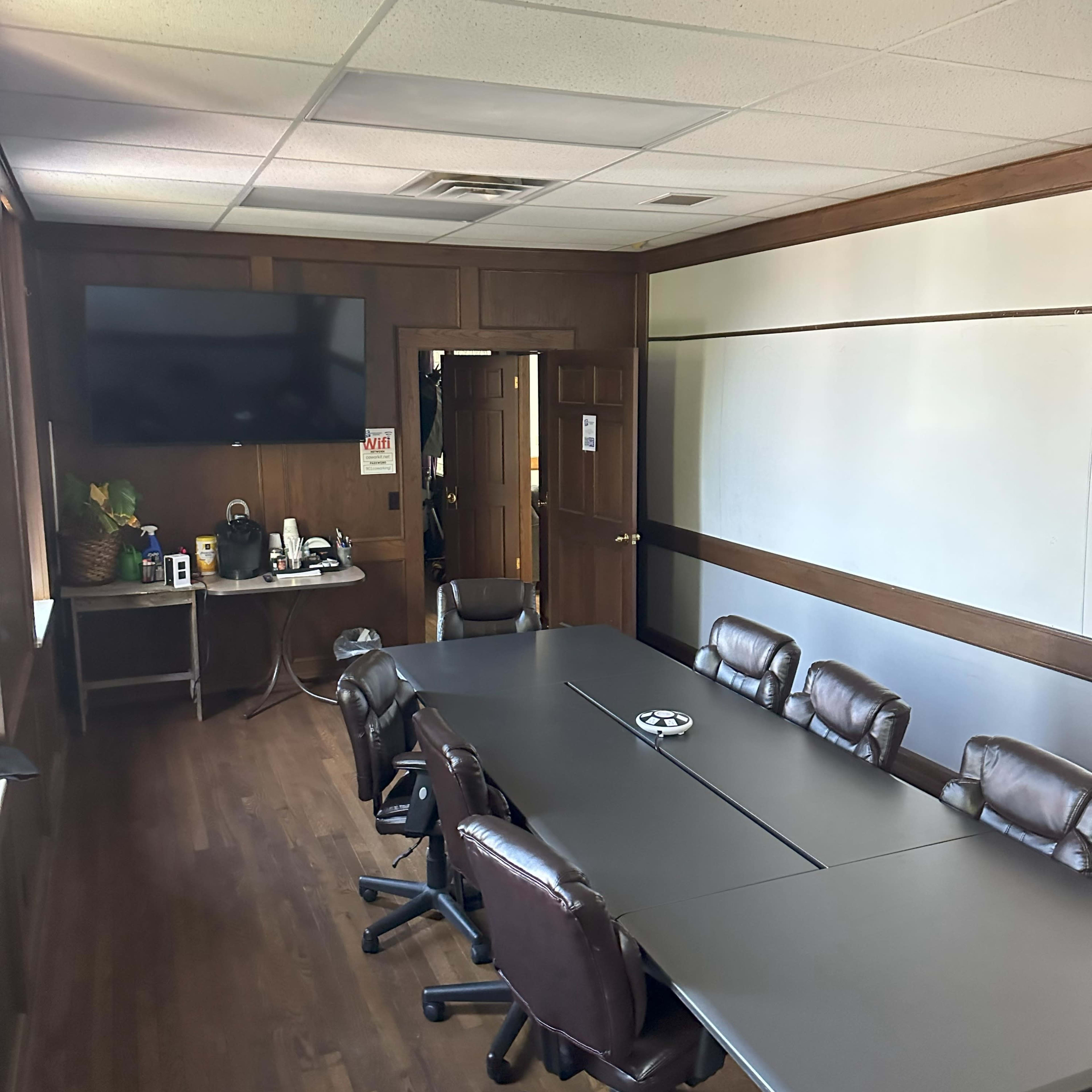 A conference room with a long table, several chairs, a wall-mounted TV, and a door leading outside.