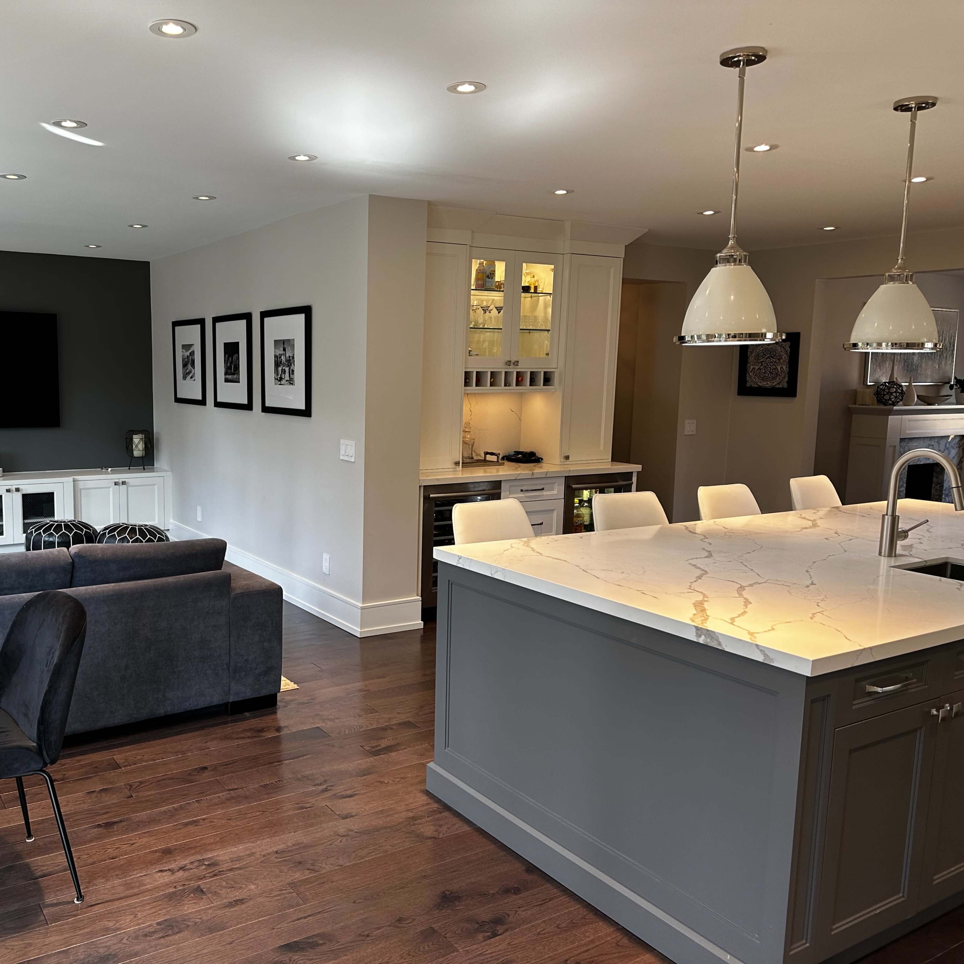 A modern open-concept kitchen and living area featuring a gray accent wall, a white storage cabinet, and a kitchen island with pendant lighting.