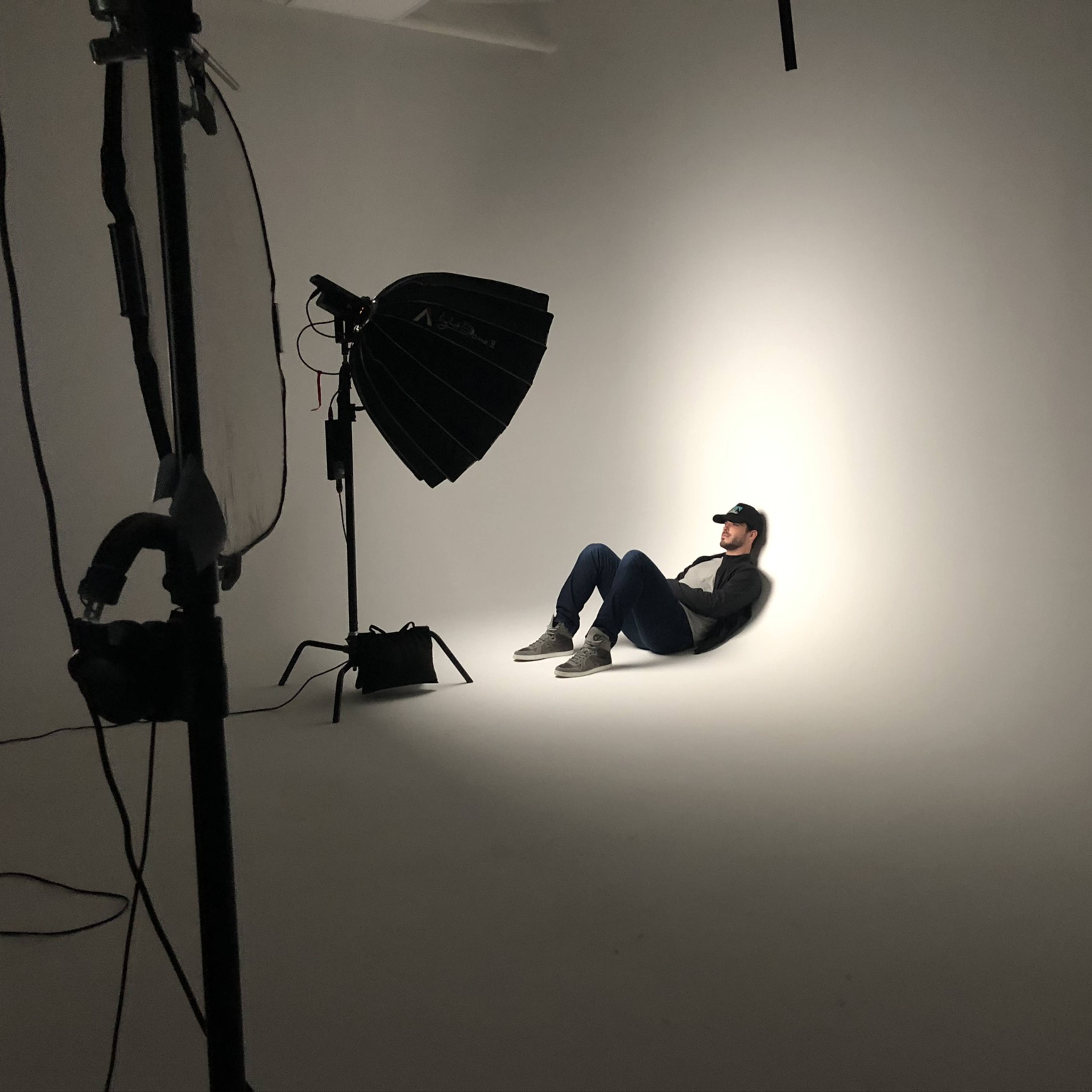 A person in a baseball cap is sitting against a white background in a photography studio.