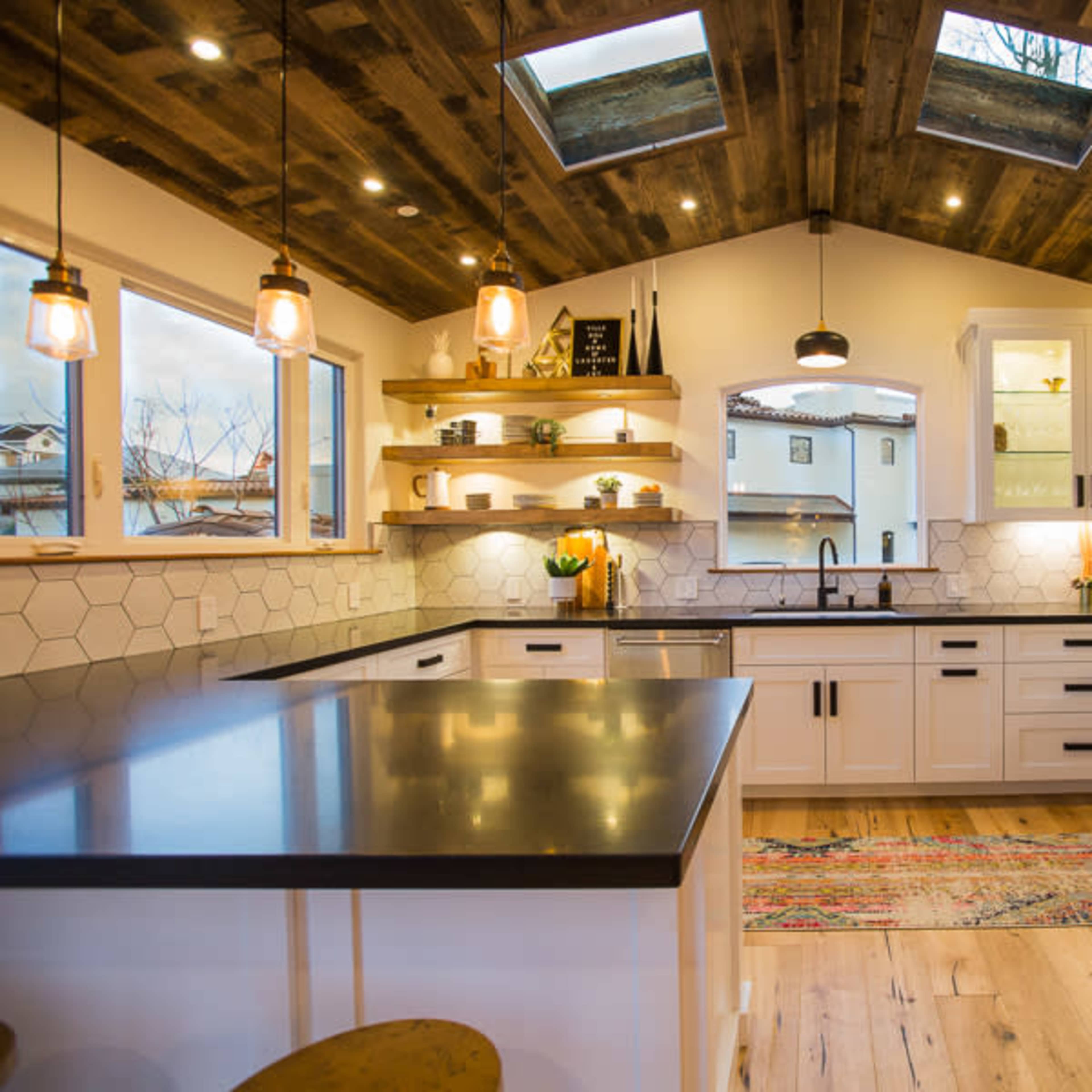 A modern kitchen features white cabinetry, a large kitchen island, hexagonal tile backsplash, and skylights illuminating the space.