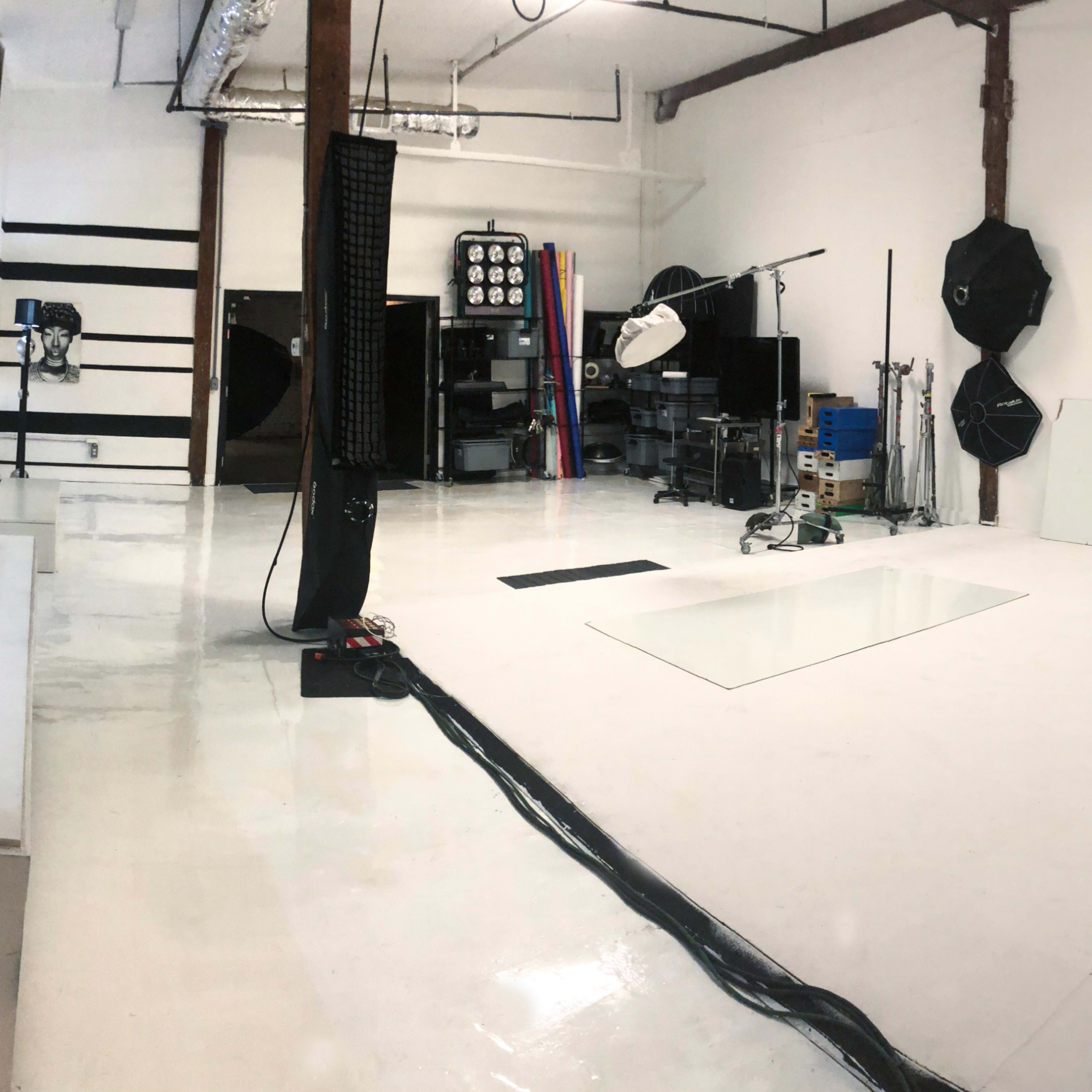 A spacious photography studio with a white floor, backdrop, and various lighting equipment set against bare walls.