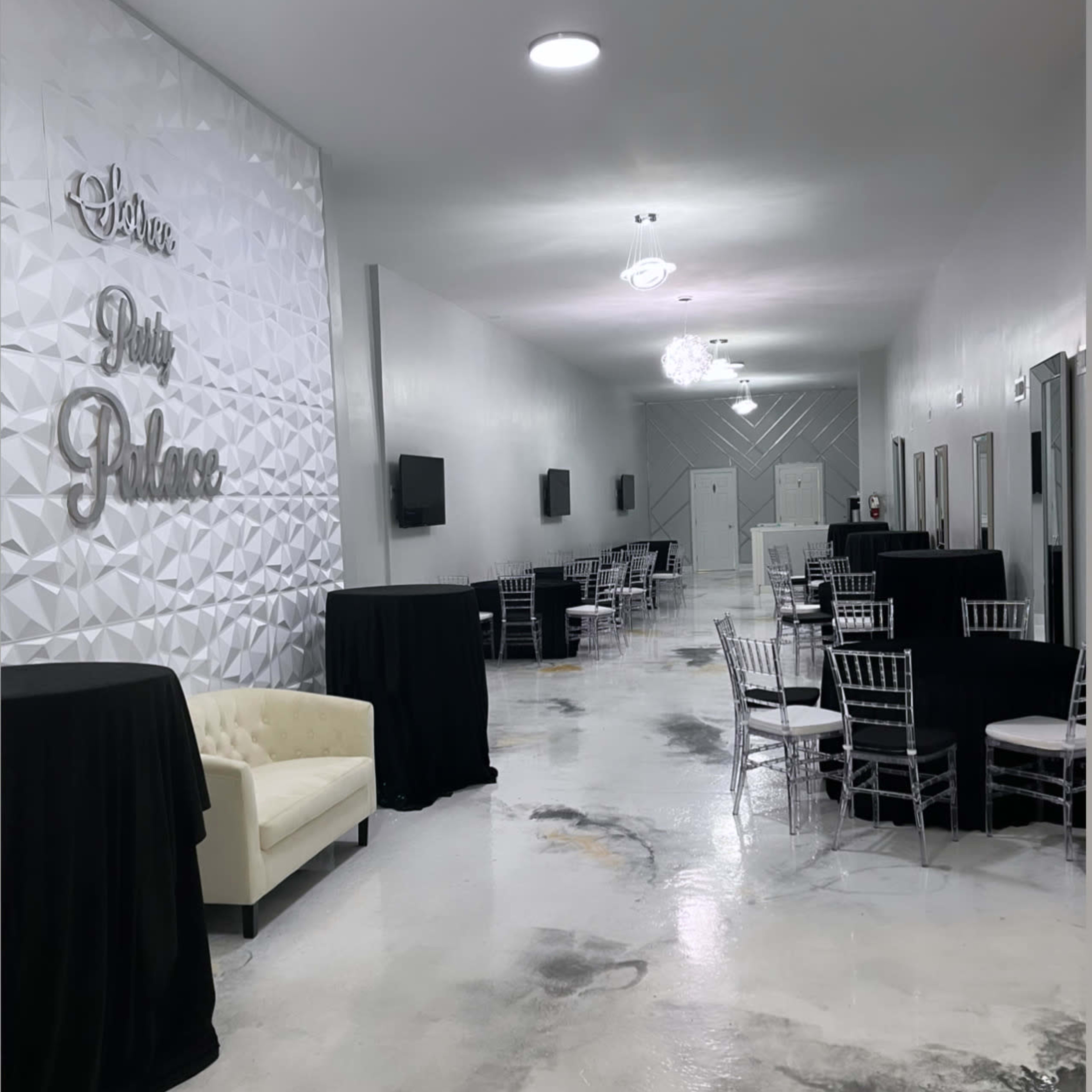 A spacious event hall with tables covered in black cloth, elegant chairs, and a decorative wall featuring the words "Party Palace."