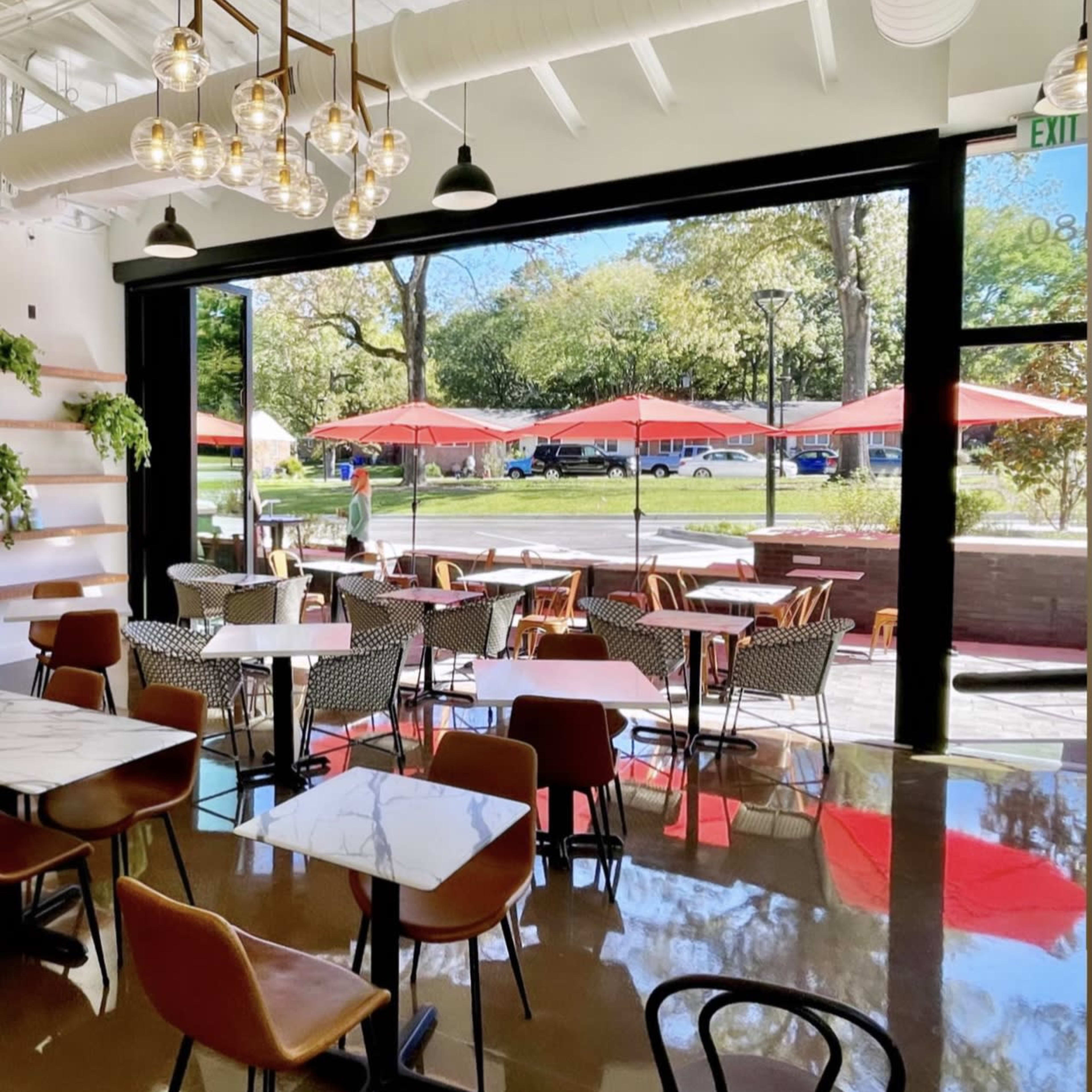 A modern café with indoor seating, large windows opening to an outdoor area with red umbrellas and greenery in Chapel Hill, North Carolina.